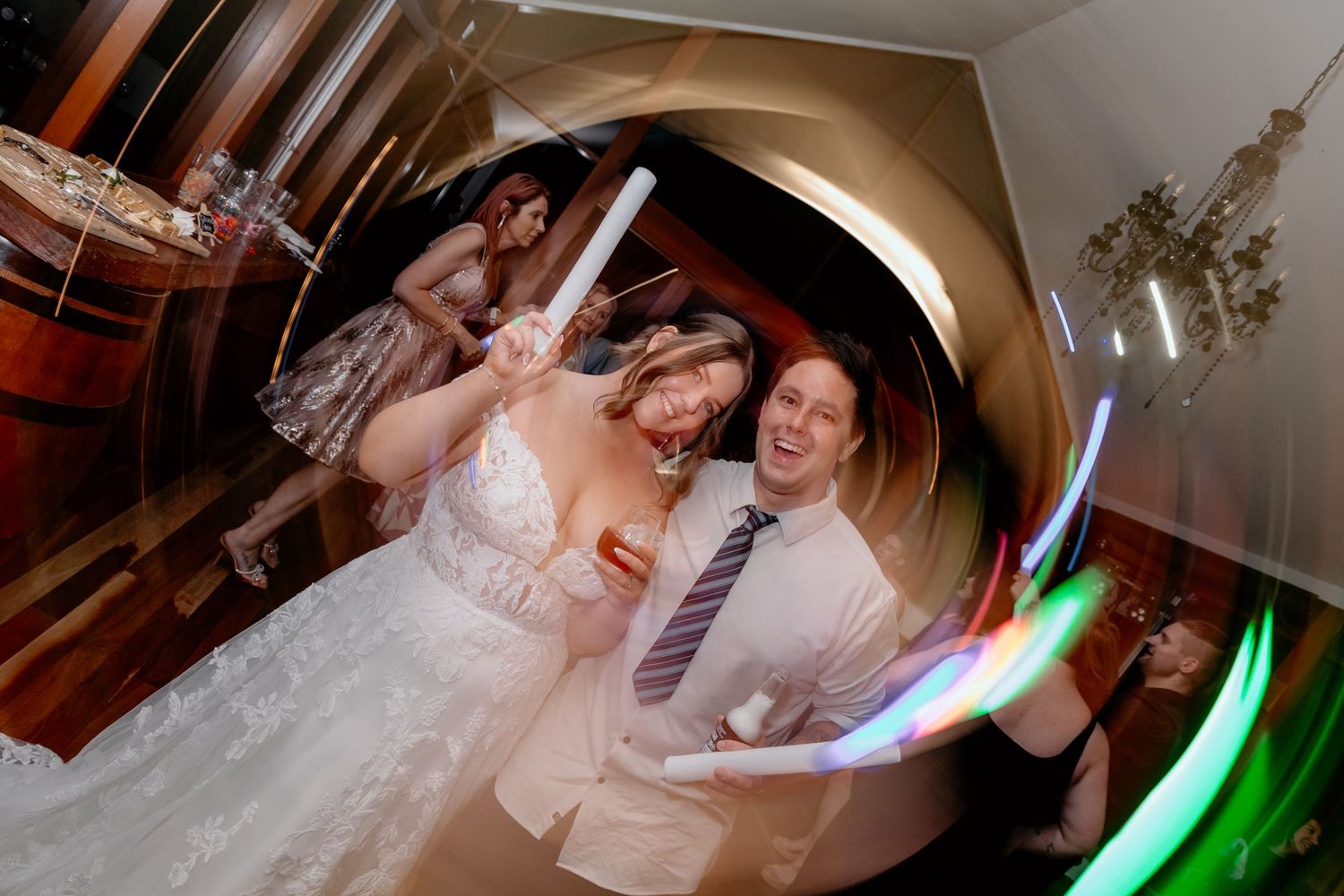 Wedding celebration captured with motion blur and colorful light trails on a dance floor at a reception venue.