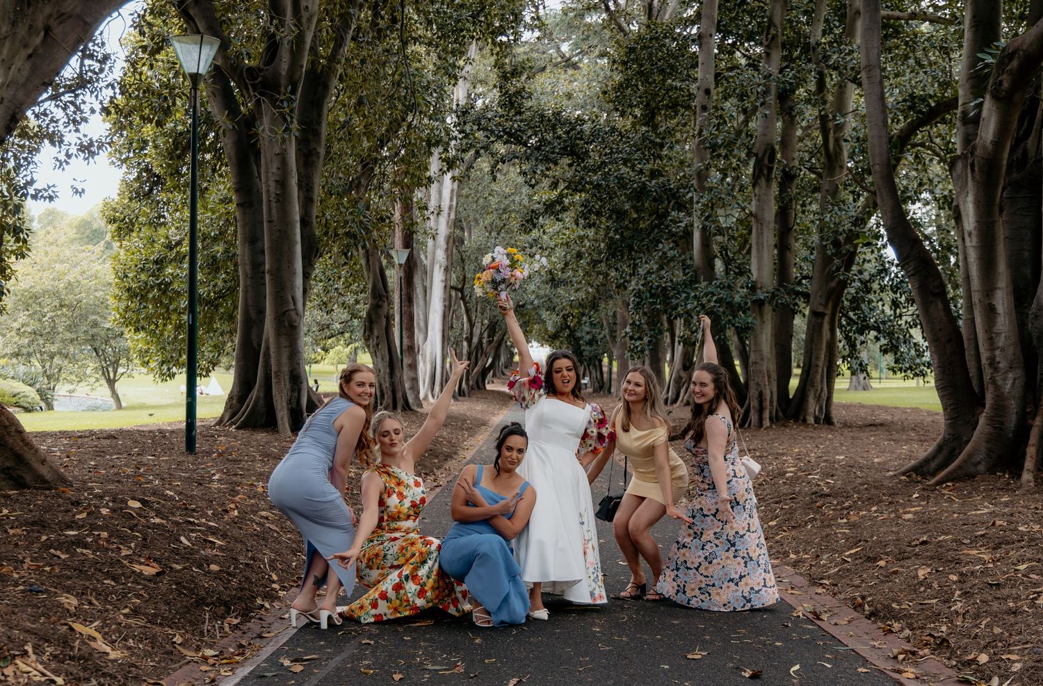 A group sits together beneath tall trees on a forest floor enjoying a sunny afternoon gathering.