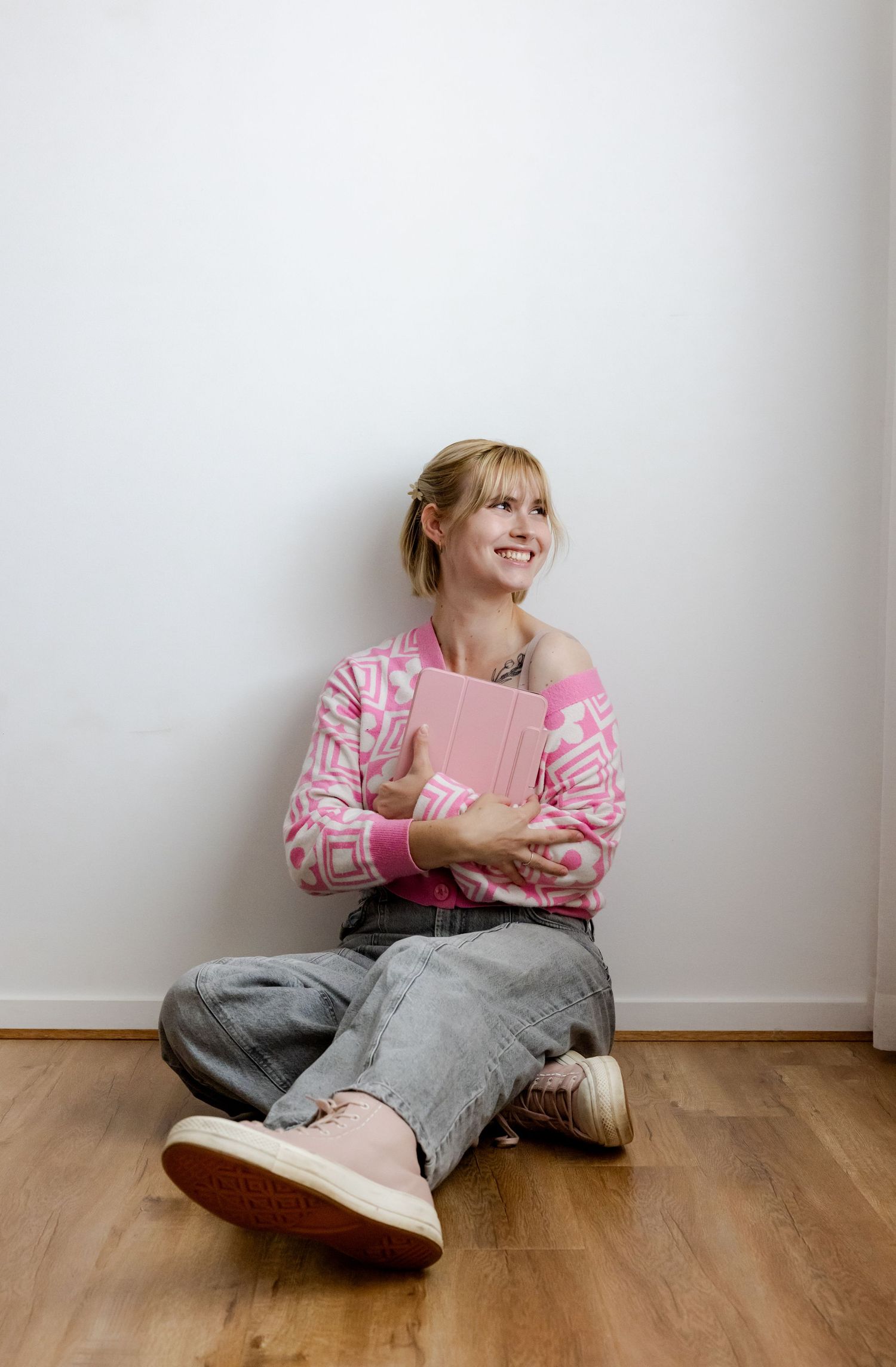 A girl in pink sits cross-legged on wooden floor holding a pink book against white wall. Gippsland photographer. Melbourne photographer.