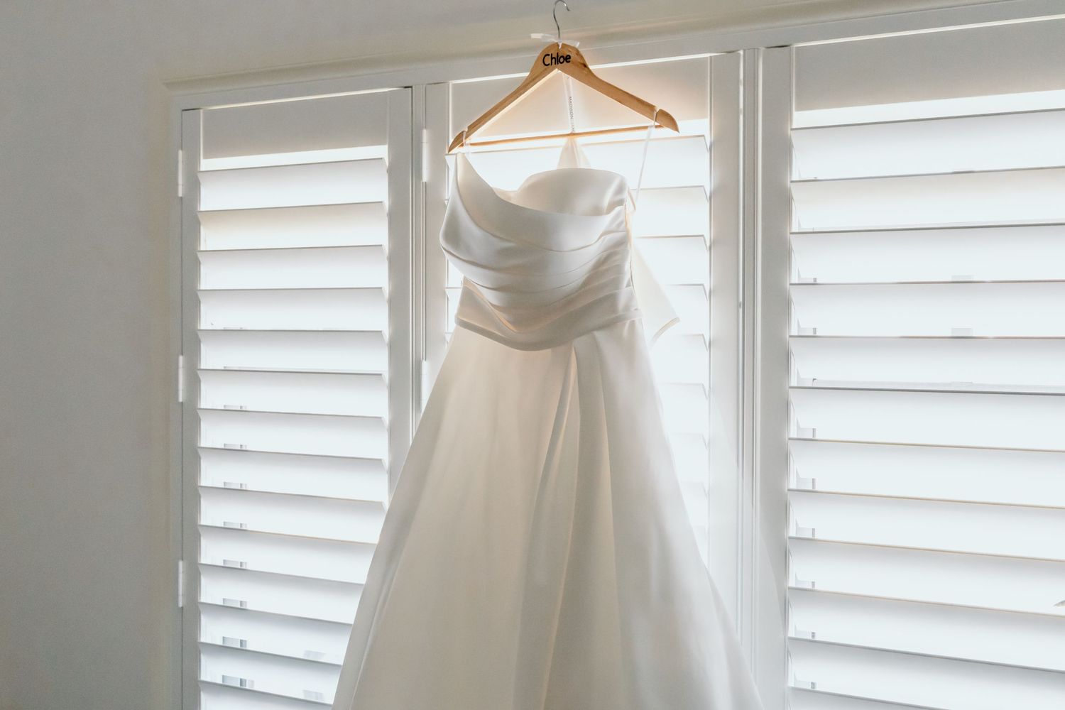 Multiple wedding dresses displayed against white shuttered windows create an elegant boutique showcase.