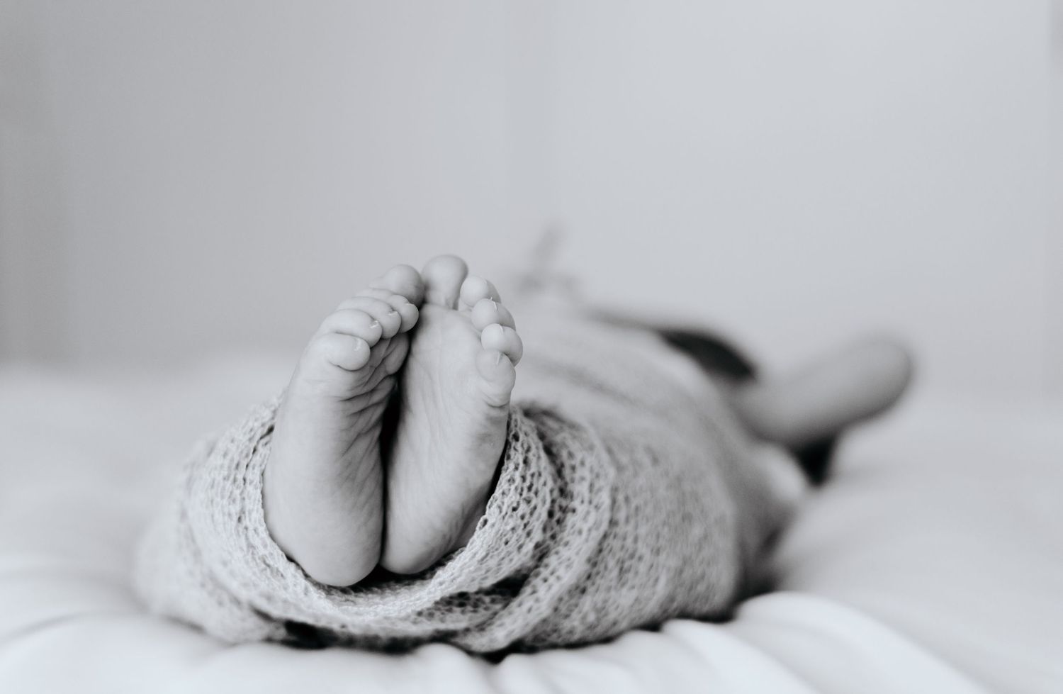 Close-up black and white detail shots of tiny baby feet and toes against white fabric.