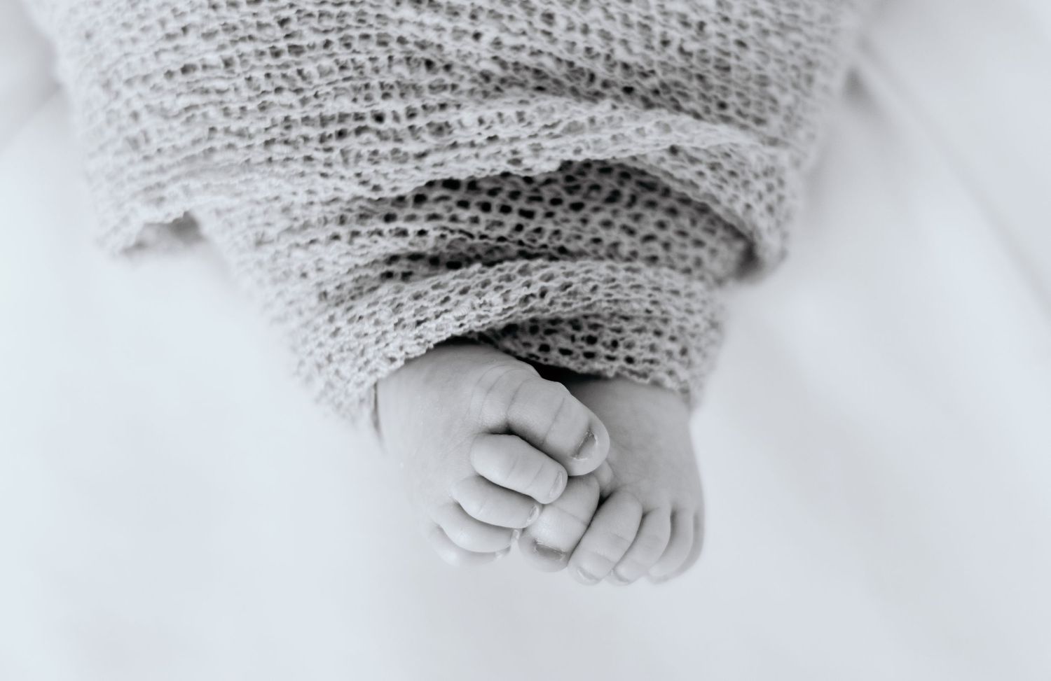 Close-up black and white image of tiny baby feet wrapped in soft knit blanket.