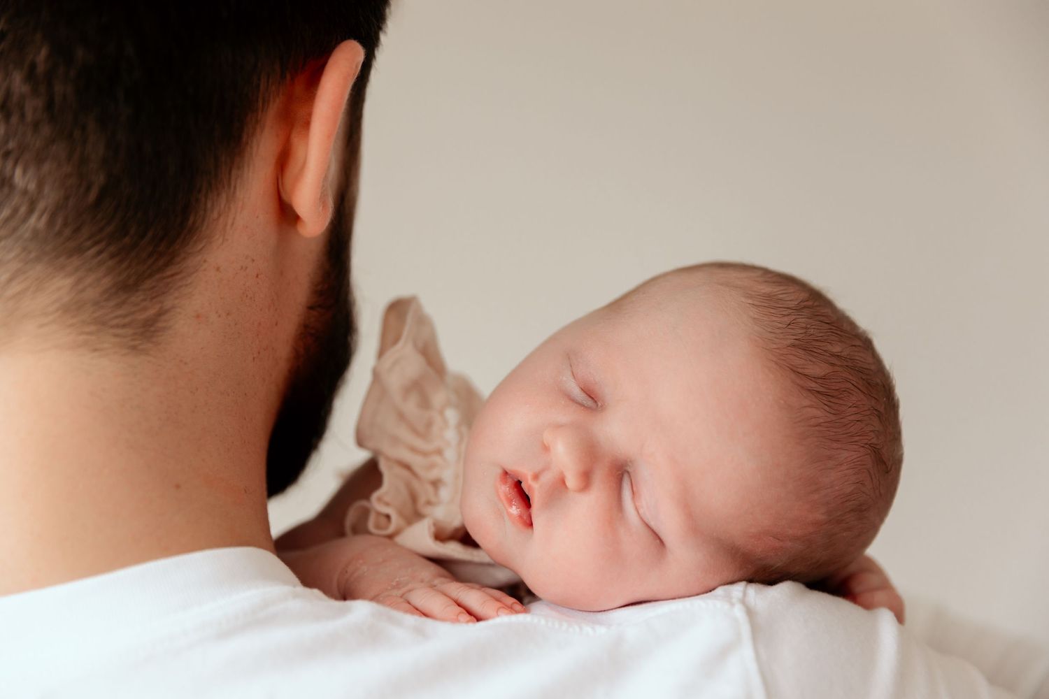 A sleeping newborn baby rests peacefully on a person's shoulder in a tender moment.