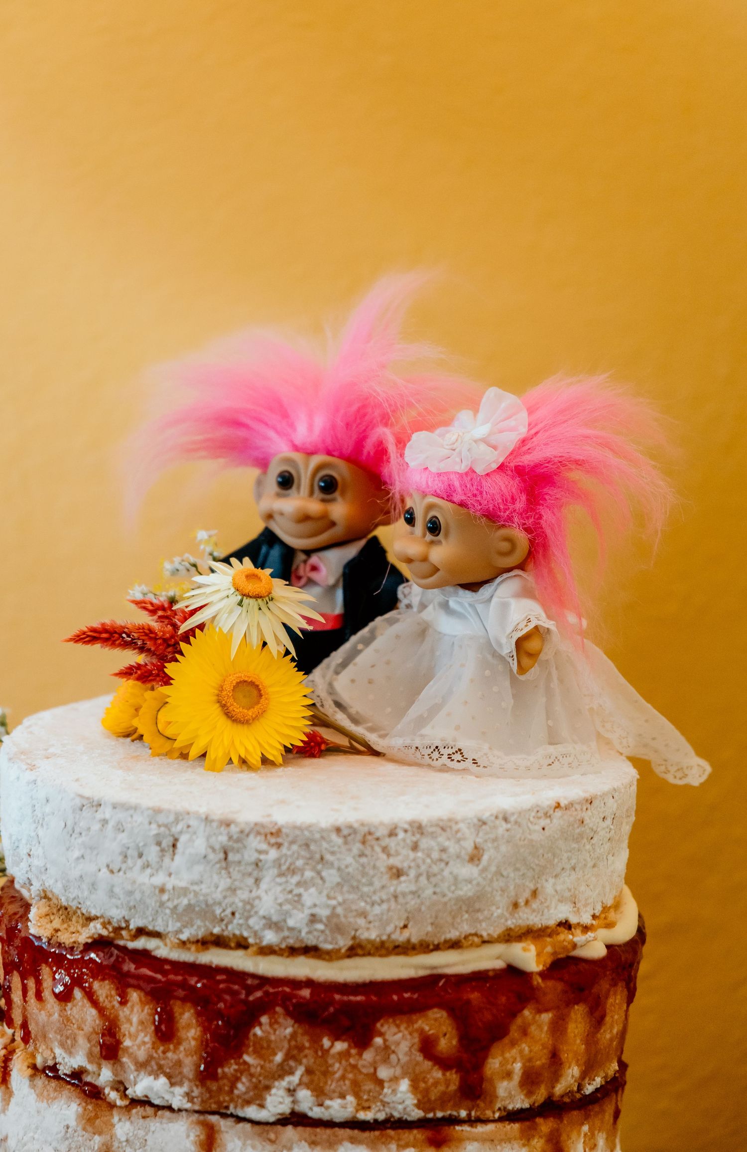 Rustic layered cake decorated with sunflowers, pink feathers and white tulle on a gold background.