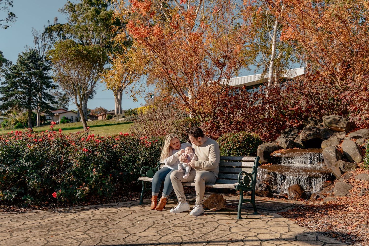 A group plays in autumn leaves on a sunny fall day at a park with colorful foliage in the background.