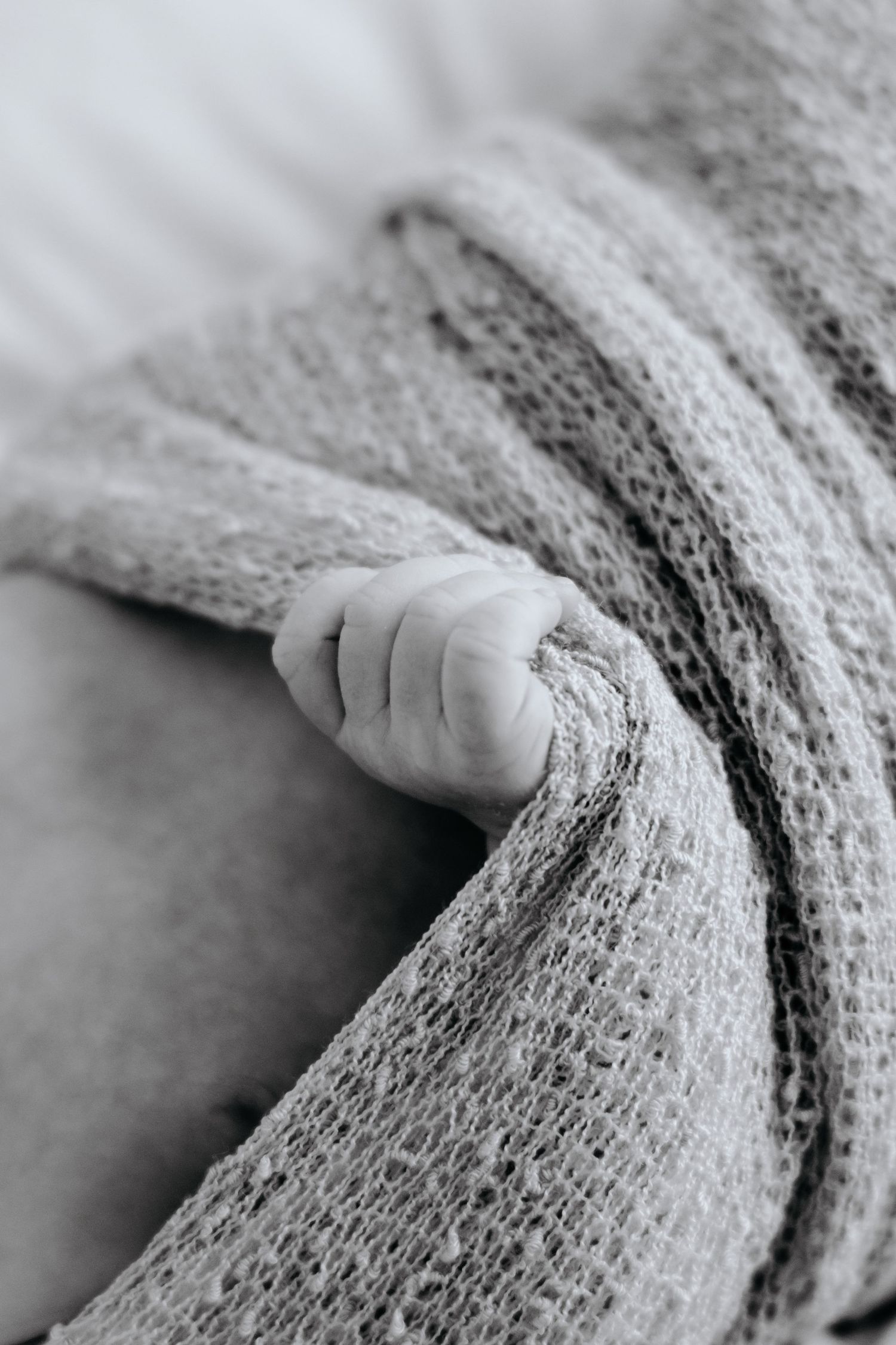 Close-up black and white image of a tiny hand grasping soft knitted fabric.
