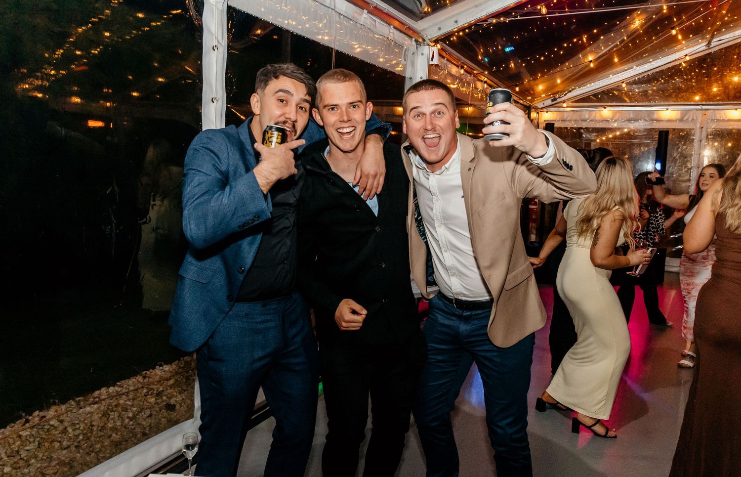 Friends celebrating at a nighttime party with drinks and festive lighting in the background.