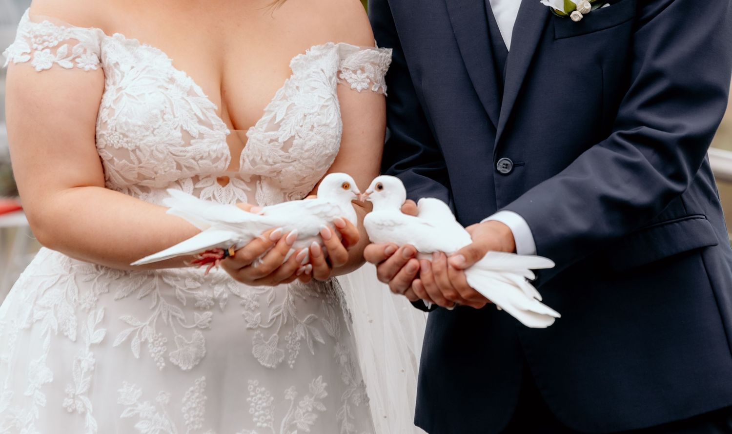 A wedding couple's hands releasing white doves into the air during their ceremony.