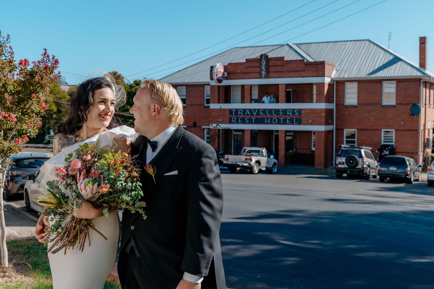 A couple shares a sweet moment outside a rustic brick building on a sunny autumn day.