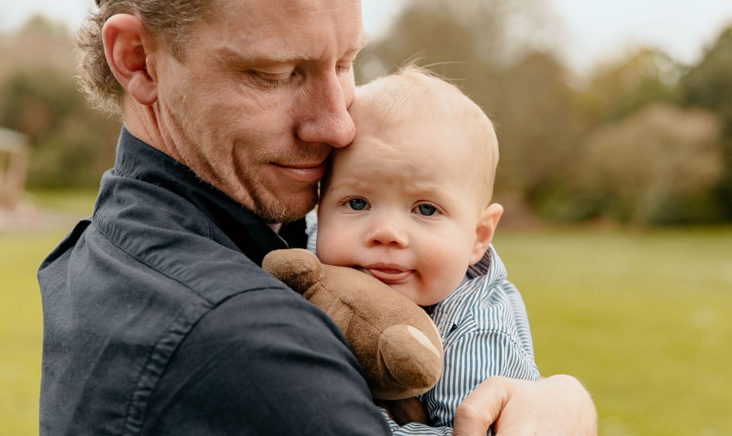Close-up of tender moment between parent and baby in outdoor setting.