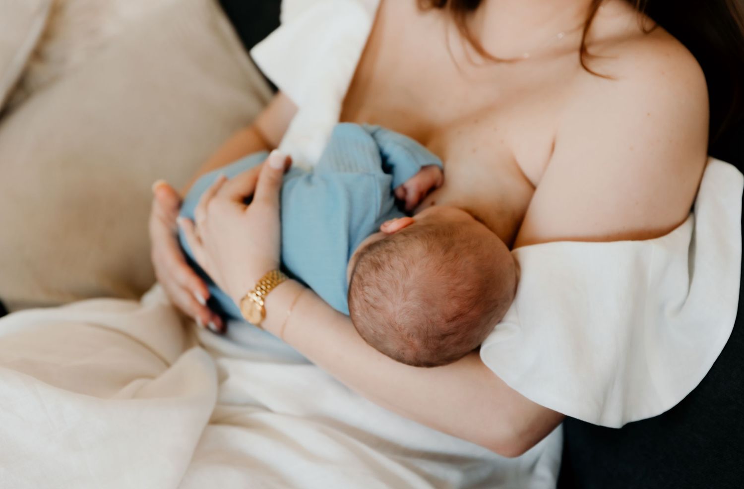 Intimate nursing moment captured in soft natural light on beige sofa.
