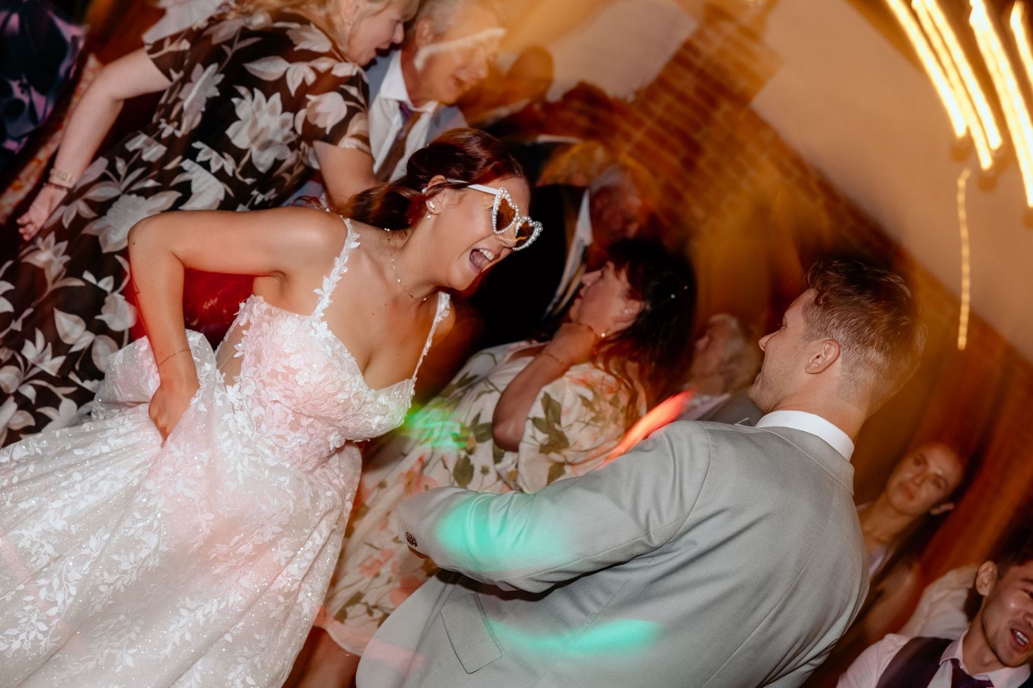 Dancing couples celebrate during a lively wedding reception with festive lighting and energetic movement on display.