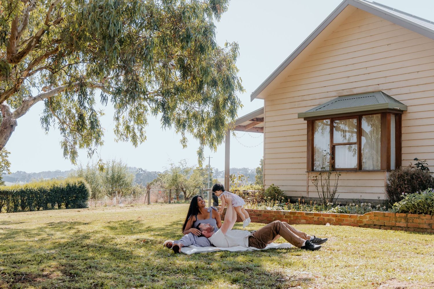 Two women relaxing on a picnic blanket in a sunny garden beside a charming country cottage.