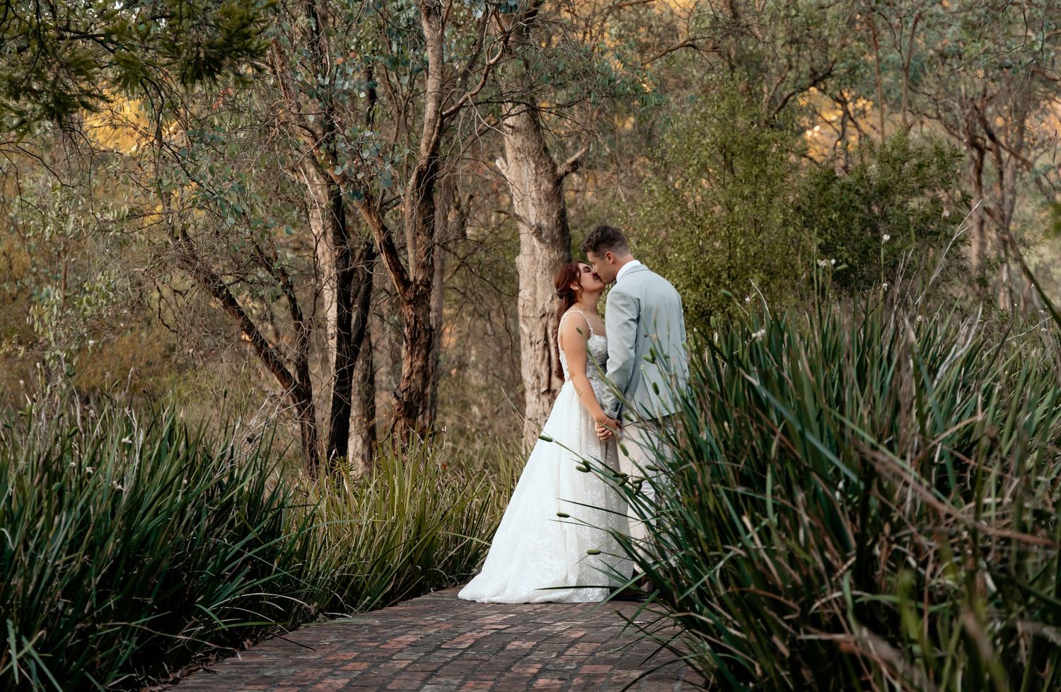 Scenic outdoor wedding ceremony setup with white chairs nestled among natural greenery at dusk.