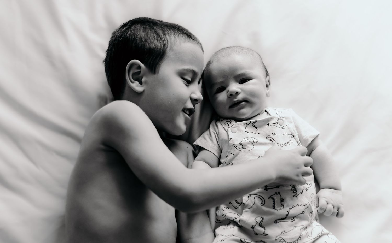A tender black and white photo series showing siblings sharing sweet moments together on white bedding.