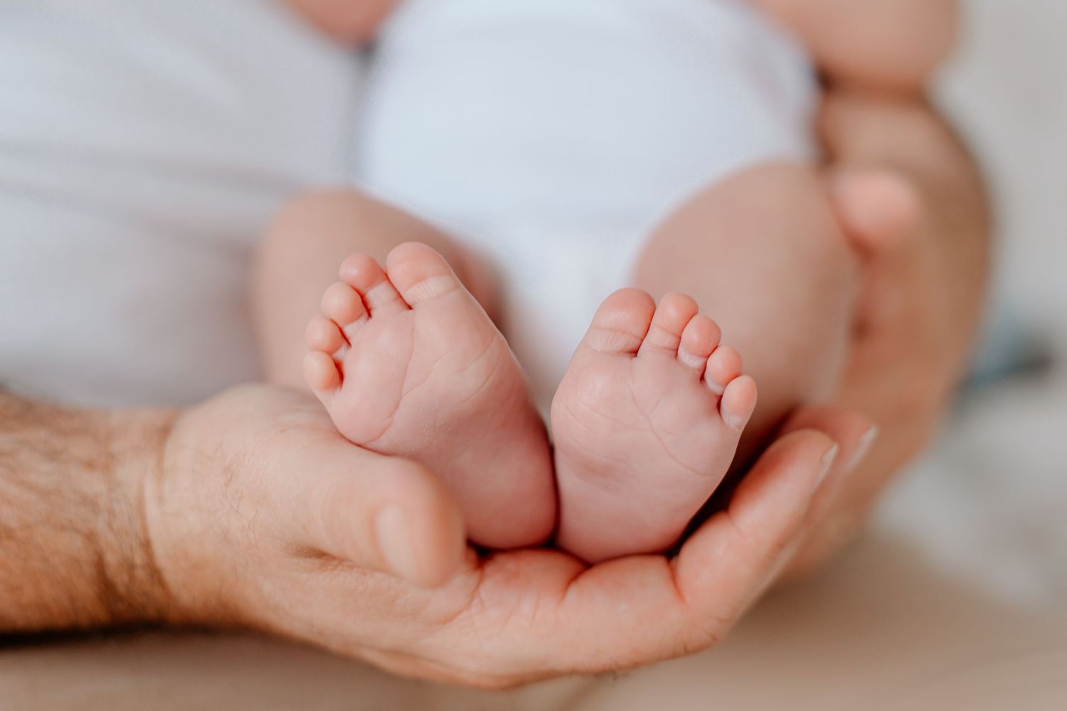 Gentle hands cradling tiny baby feet against a white background.