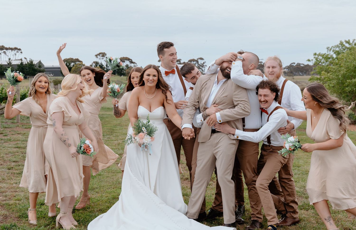 Wedding party in neutral tones celebrates outdoors with joyful expressions and candid moments during photo session.