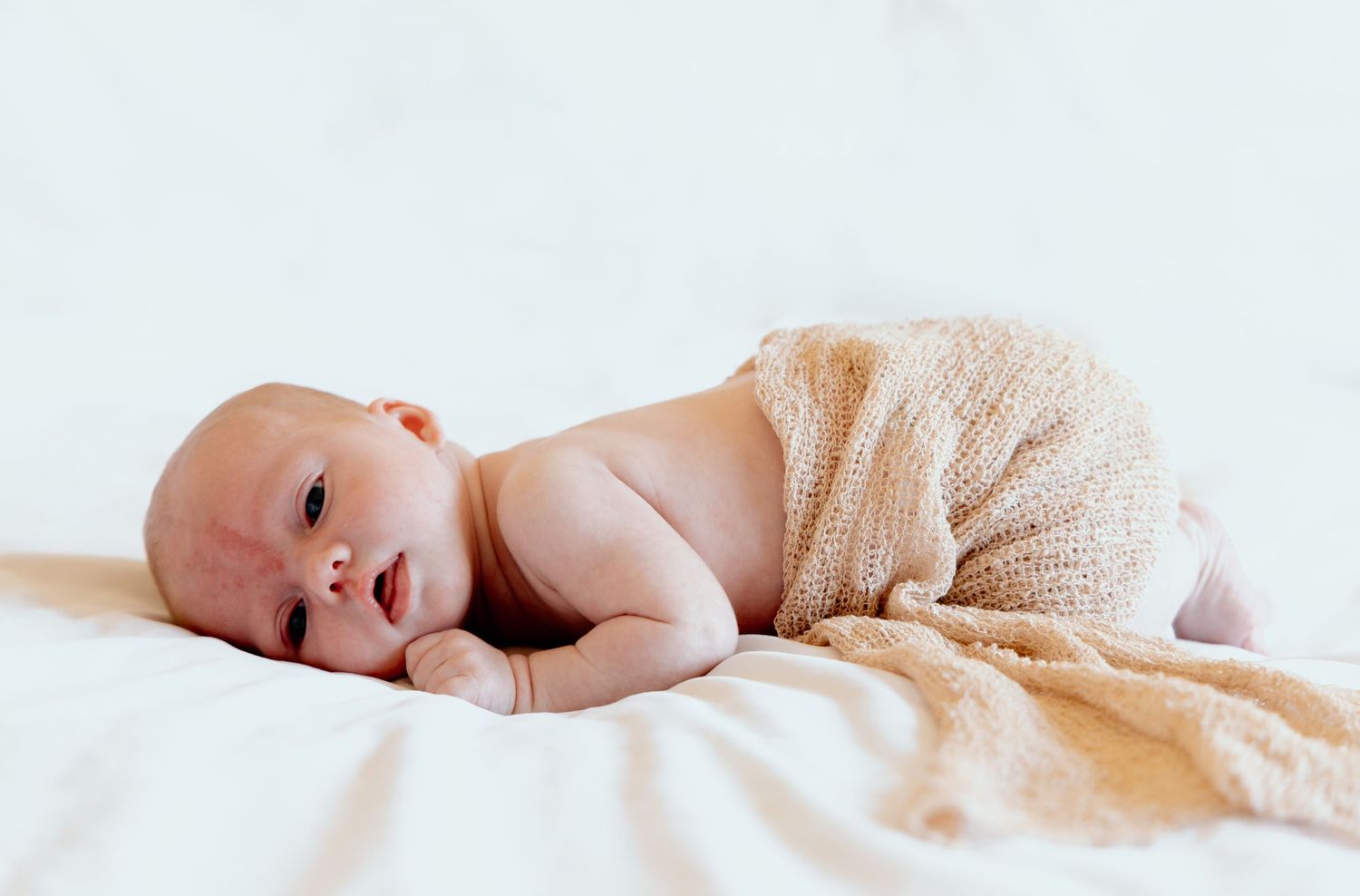 Newborn baby sleeping peacefully under soft beige blanket in natural light setting.
