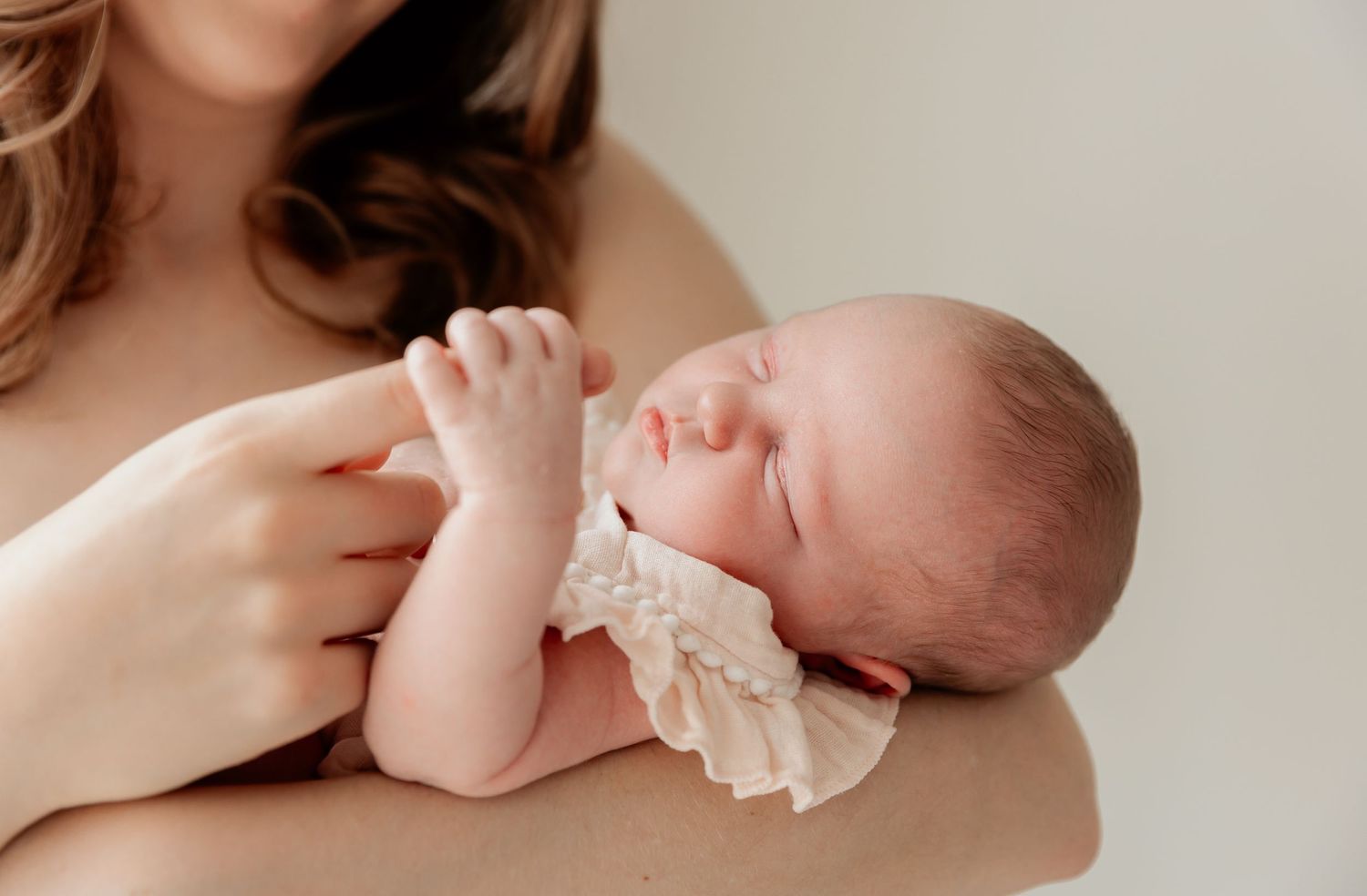 Tender moment of baby in white lace dress resting against caregiver.