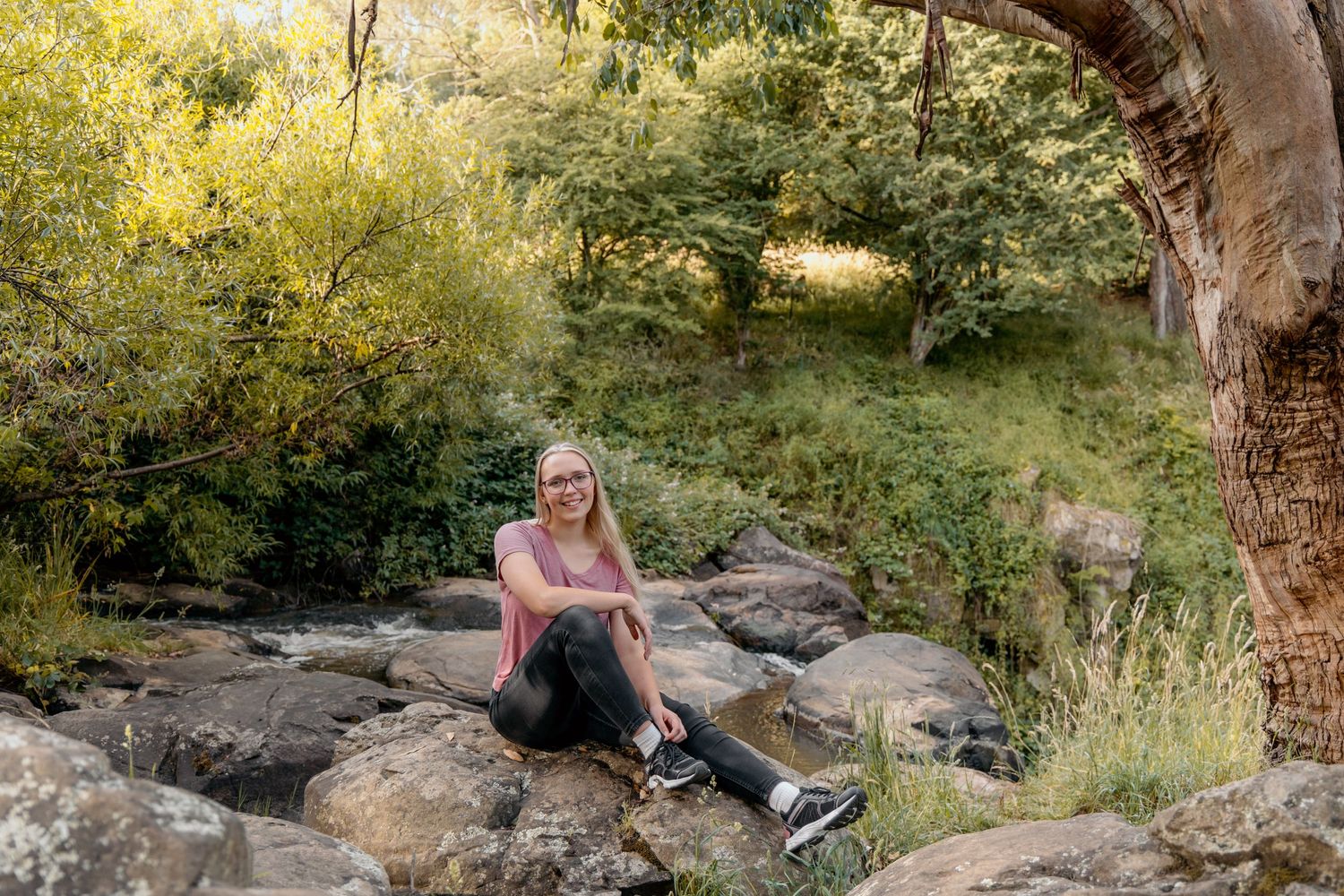Person relaxing on rocky outcrop under curved tree branch in natural setting.