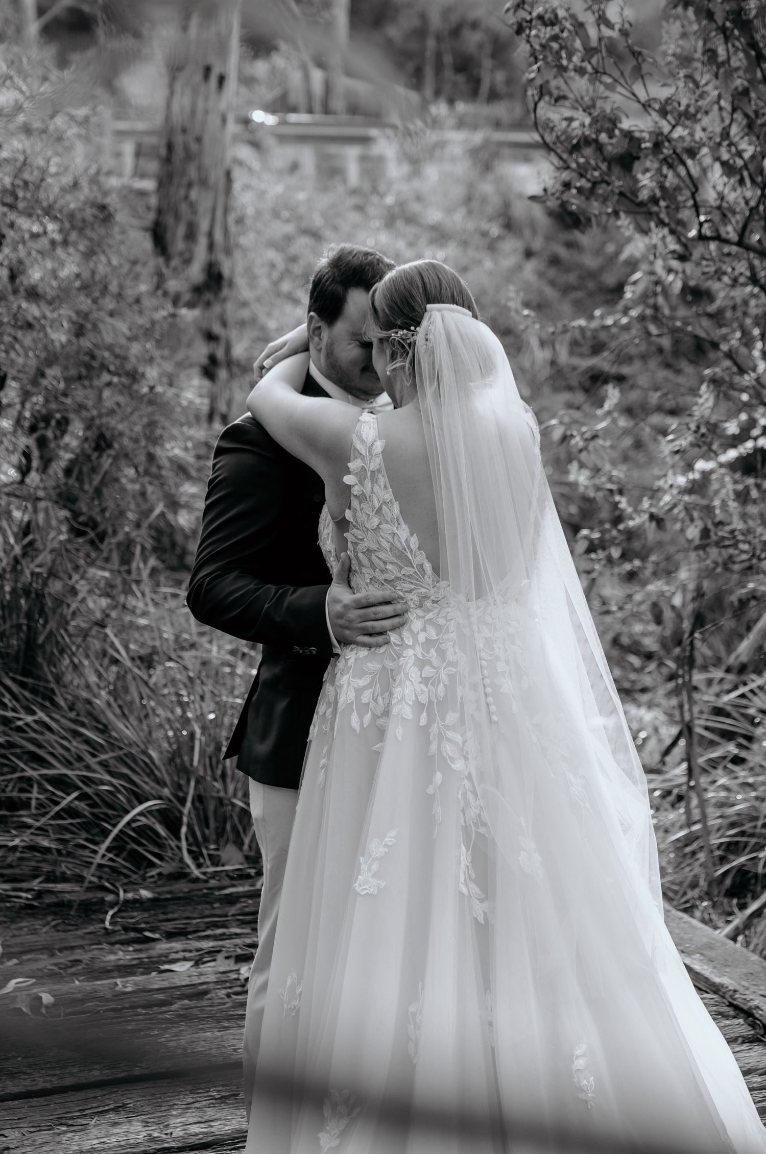 A romantic black and white photo series of a couple embracing during their wedding, with a veil flowing in the breeze.