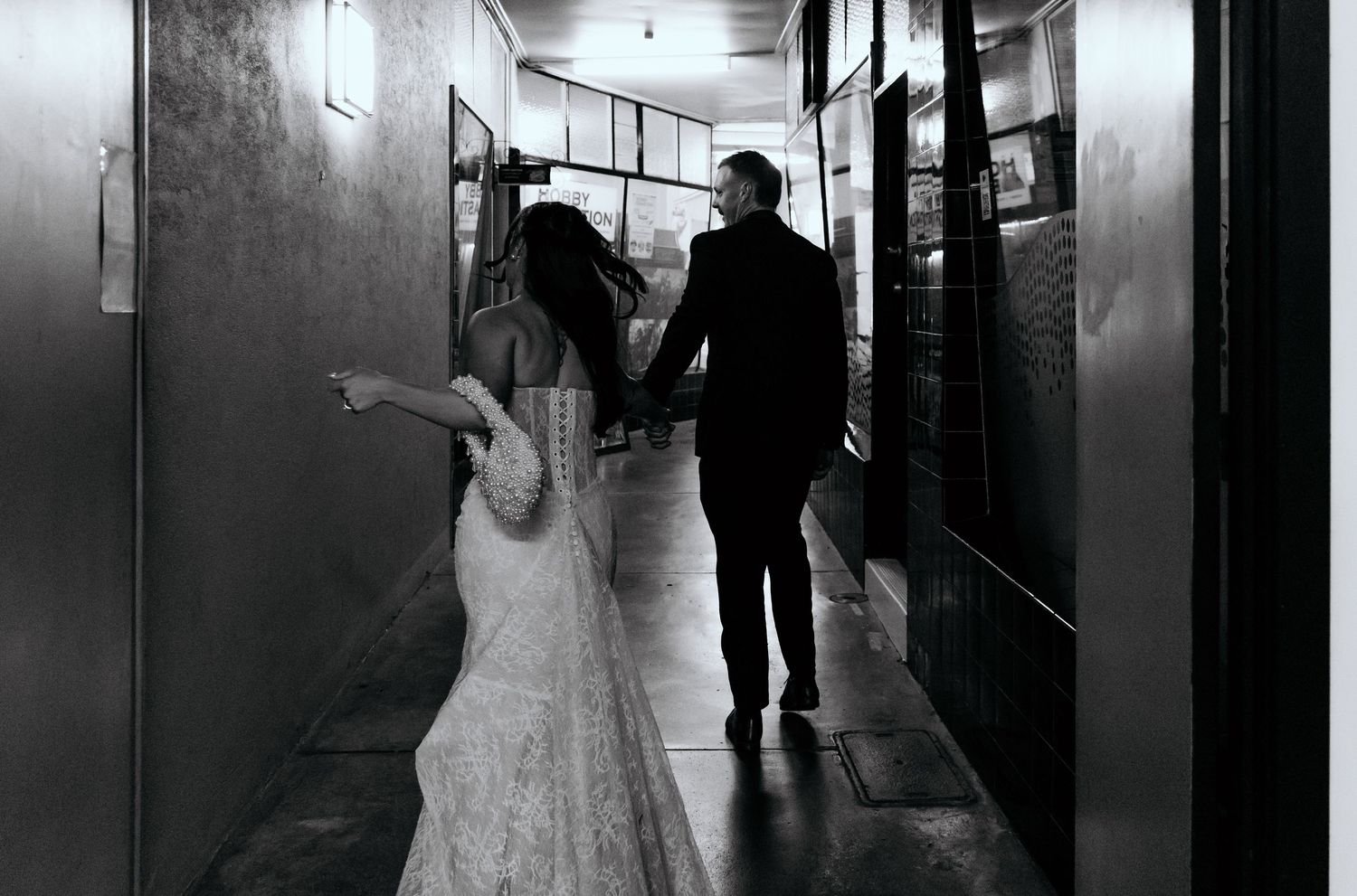 Black and white photo of a bride and groom walking hand in hand down a hallway on their wedding day.