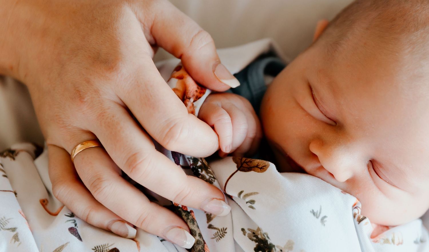 Close-up of tiny baby hand being held against patterned fabric.