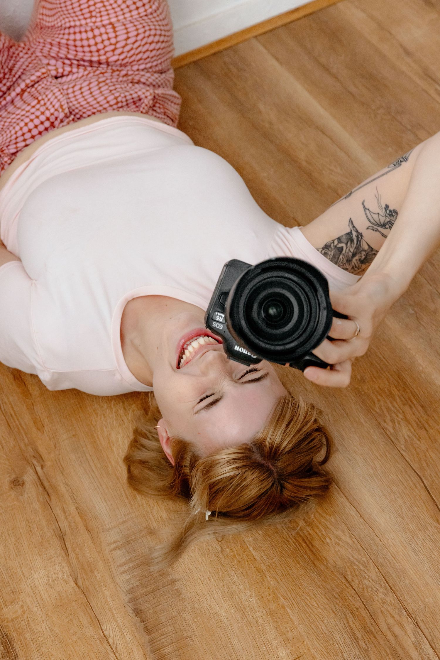 A photographer lies on wooden floor holding camera up while wearing red and white outfit. Gippsland photographer. Melbourne photographer.
