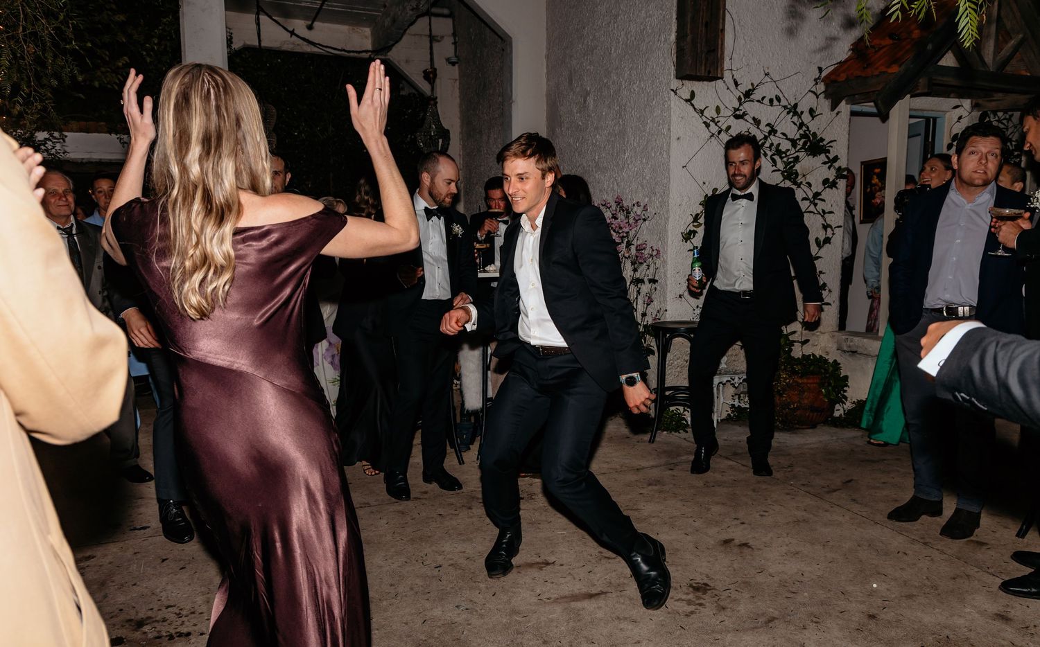 Wedding guests dancing energetically at lively outdoor evening reception celebration.