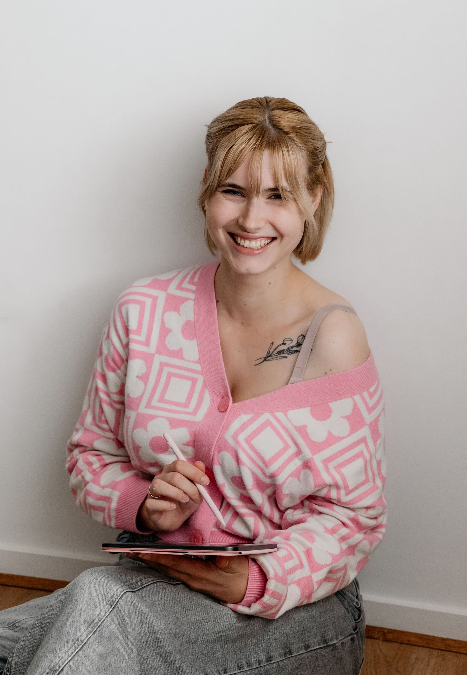 A photographer in pink sweater smiles while holding digital tablet against white wall. Gippsland photographer. Melbourne photographer.