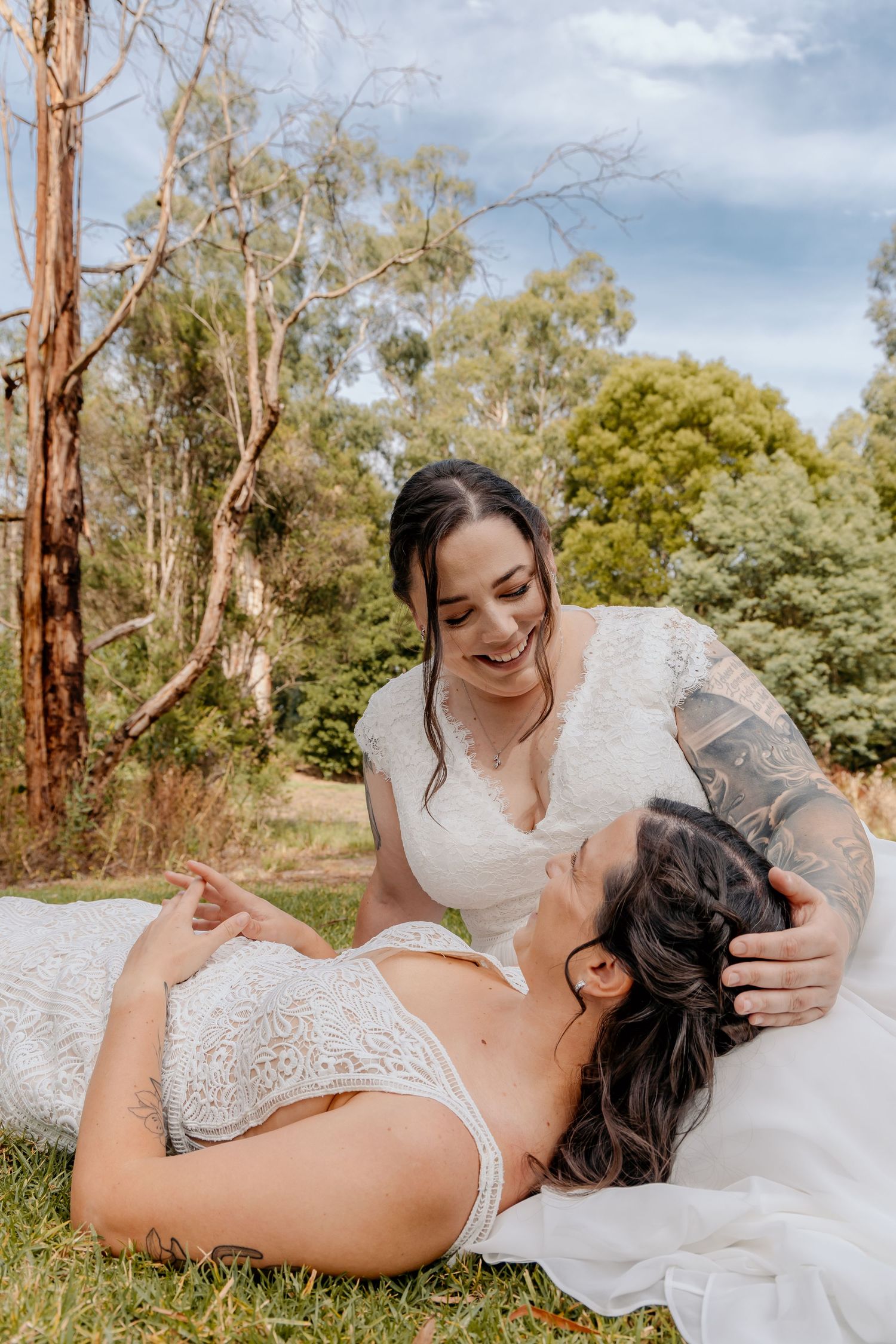 A romantic outdoor photoshoot in nature with two people in white lace dresses laying in the grass among eucalyptus trees.