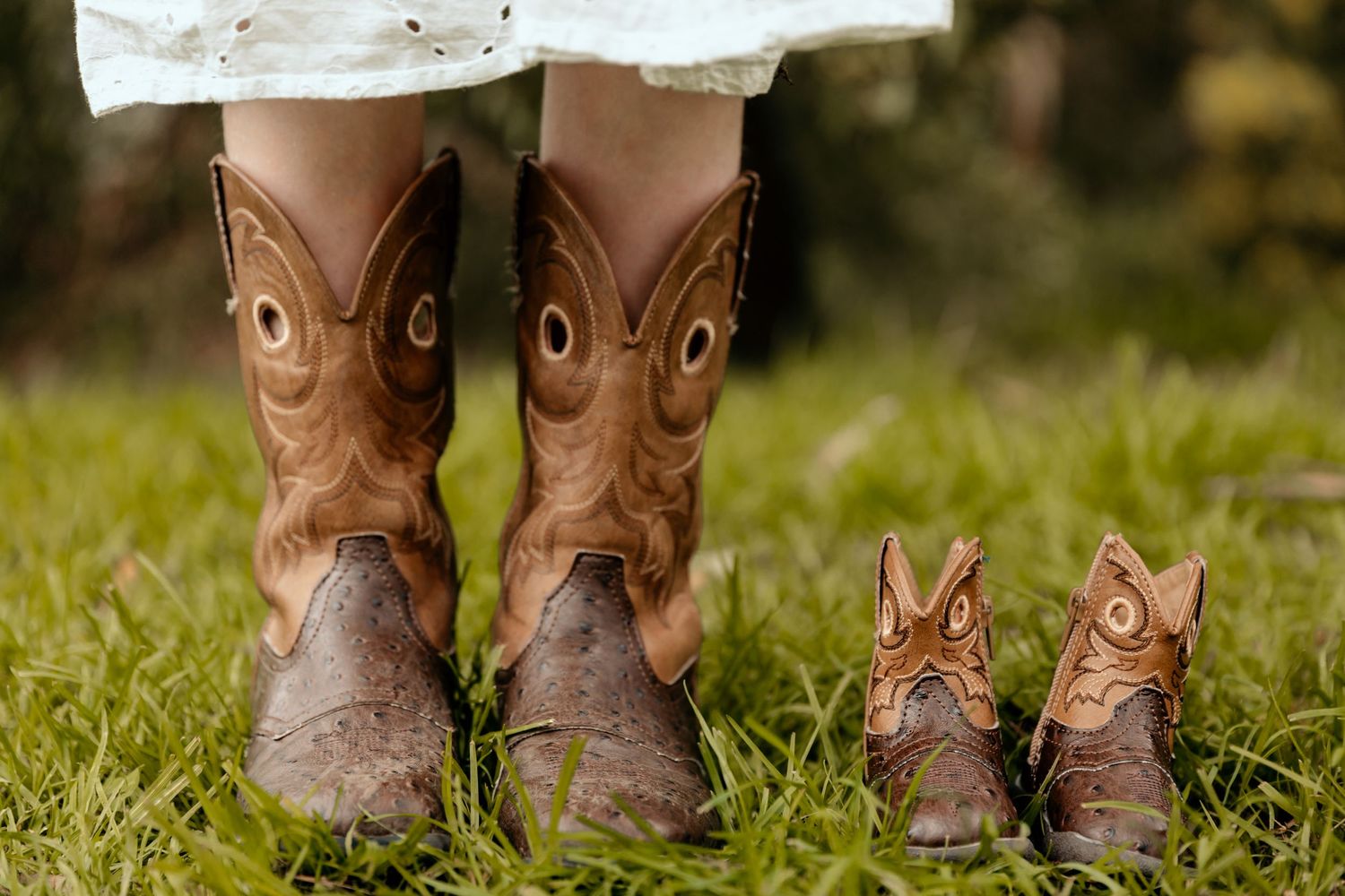 Brown cowboy boots with matching miniature baby boots on grass.