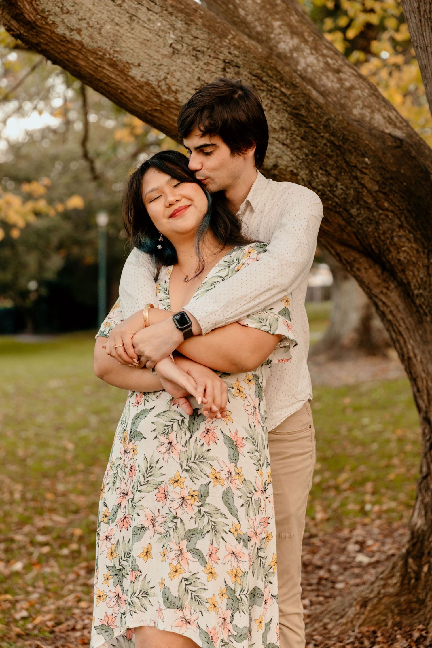 A romantic couple embraces under an autumn tree with the woman wearing a floral dress. Gippsland photographer. Melbourne photographer.