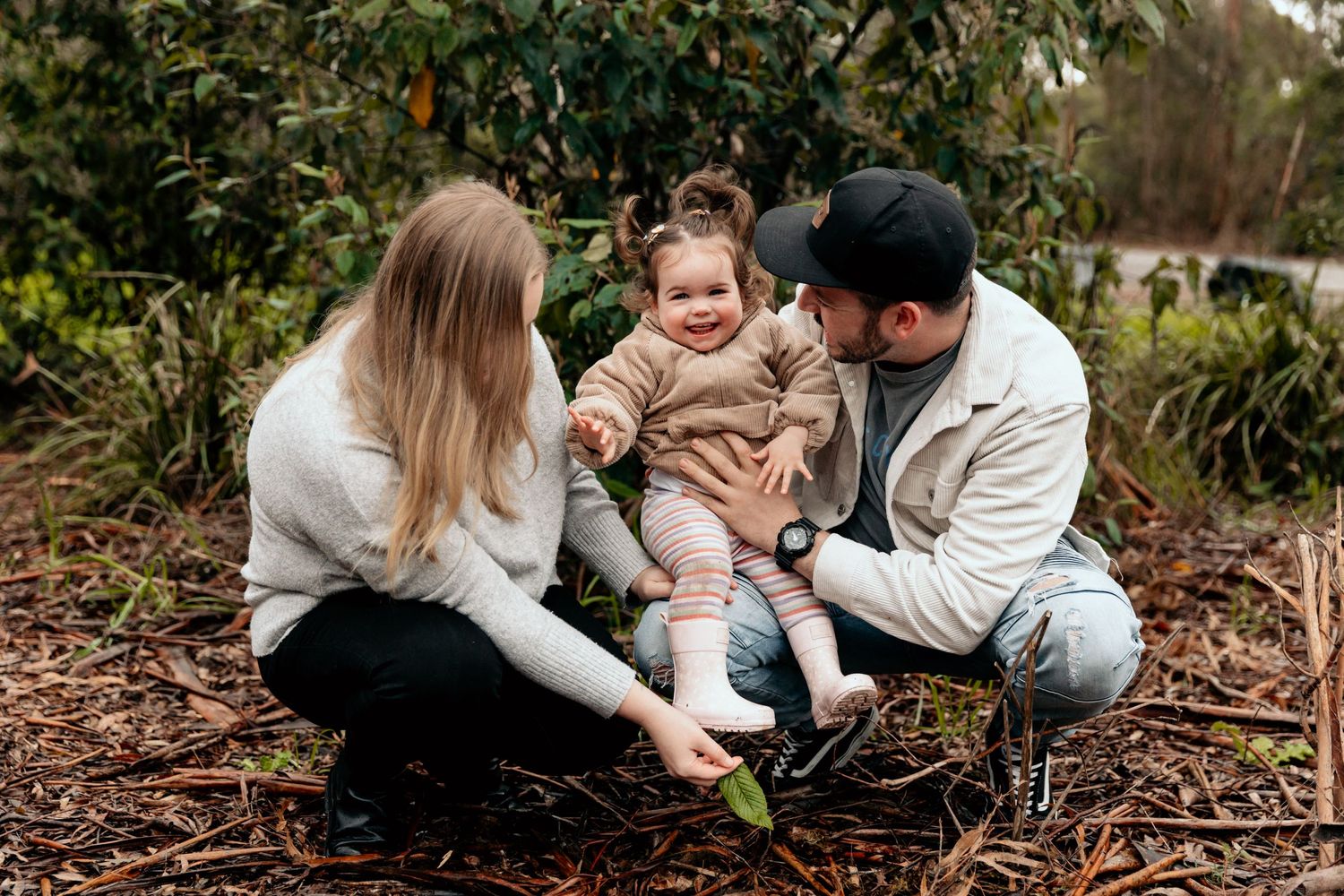 Family sitting together on ground during outdoor photo session.