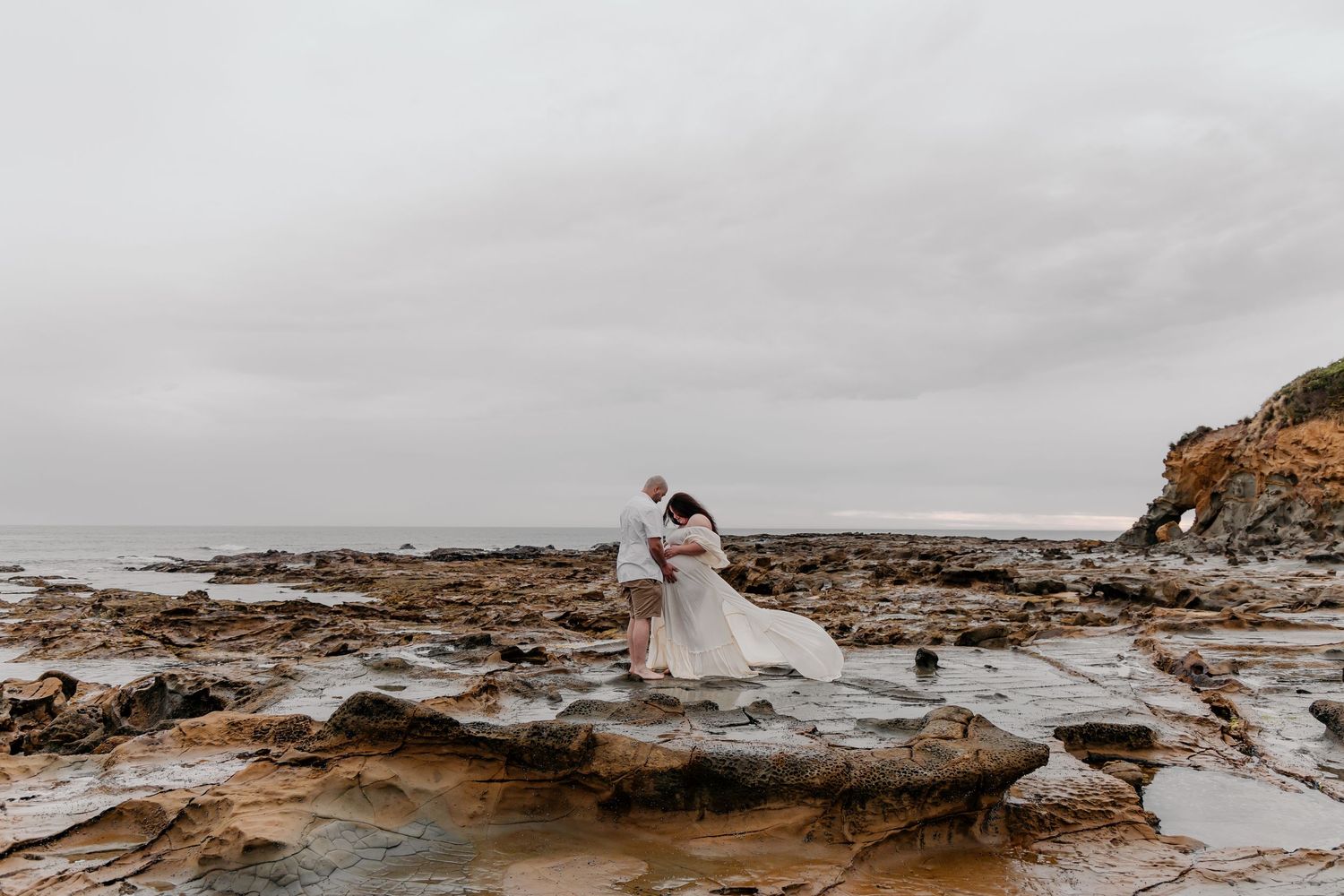 A moody coastal seascape with rocky cliffs and crashing waves under an overcast sky.