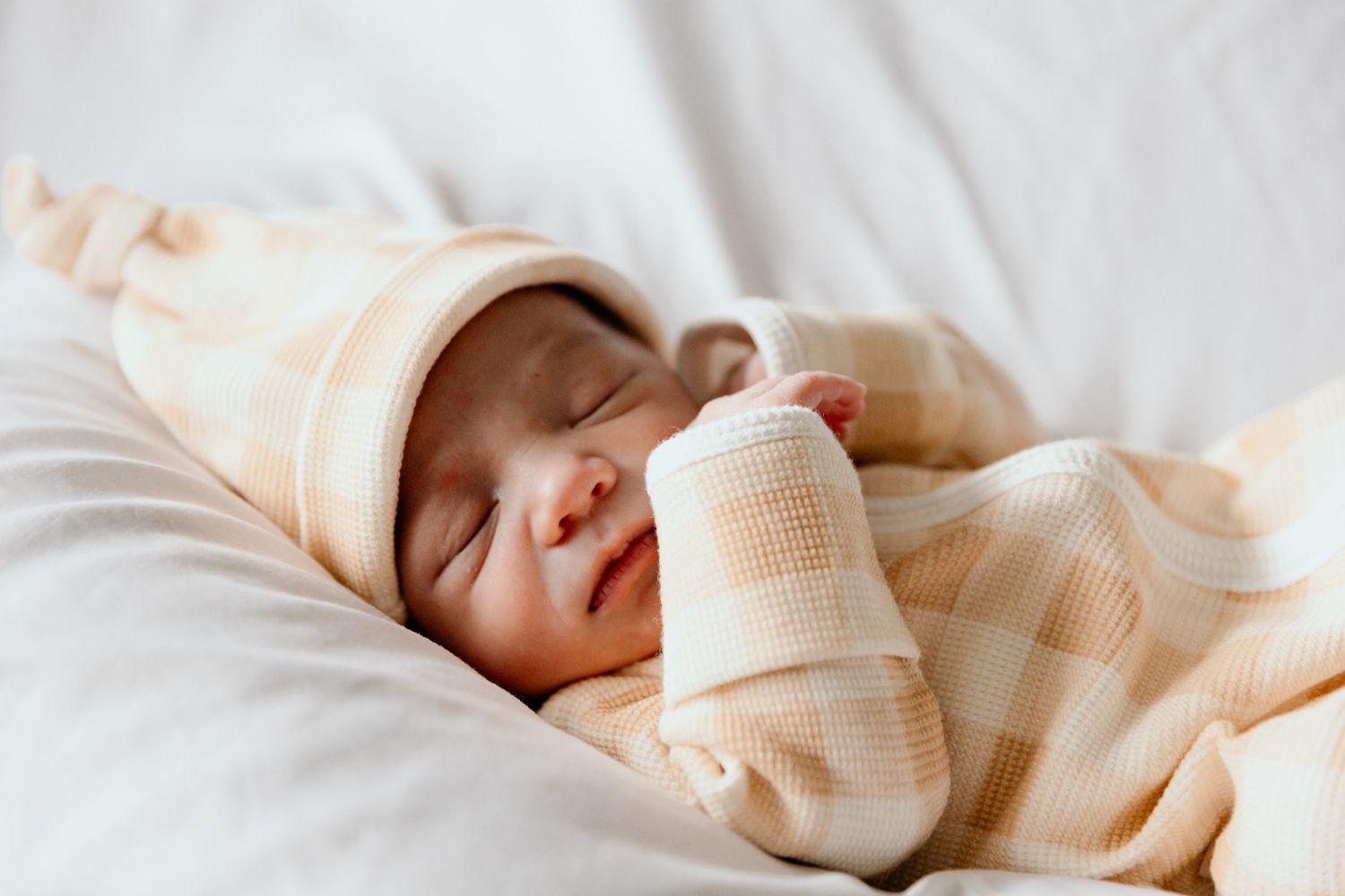 Sleeping newborn baby wearing cream colored hat and swaddled in matching blanket.