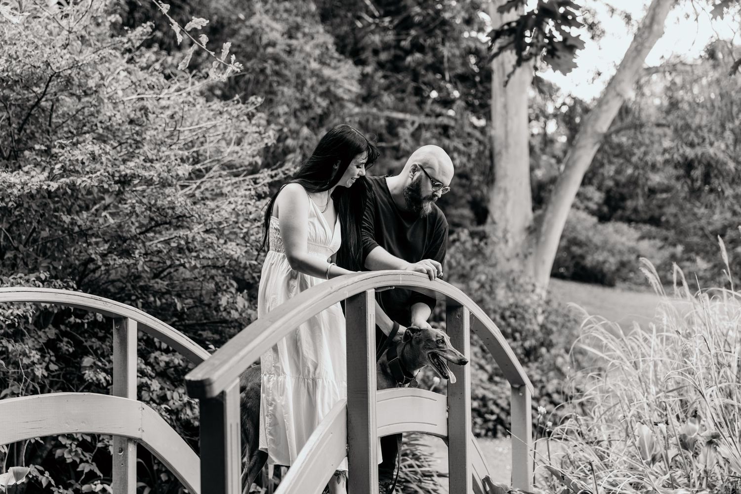 Black and white portrait of couple on decorative garden bridge among trees.