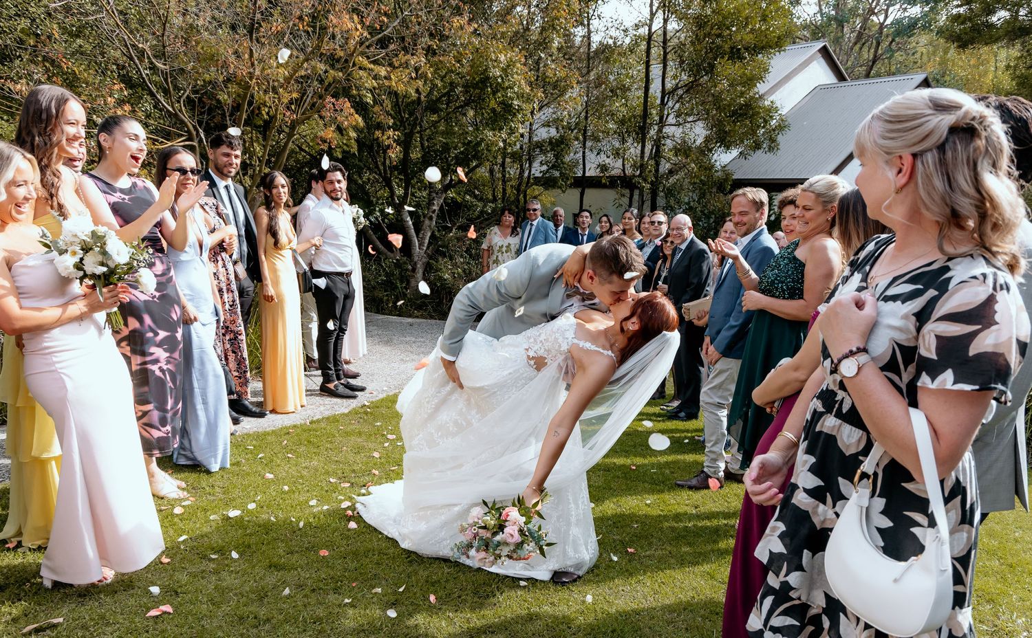 Wedding guests toss flower petals during an outdoor garden ceremony as the couple walks down the aisle.