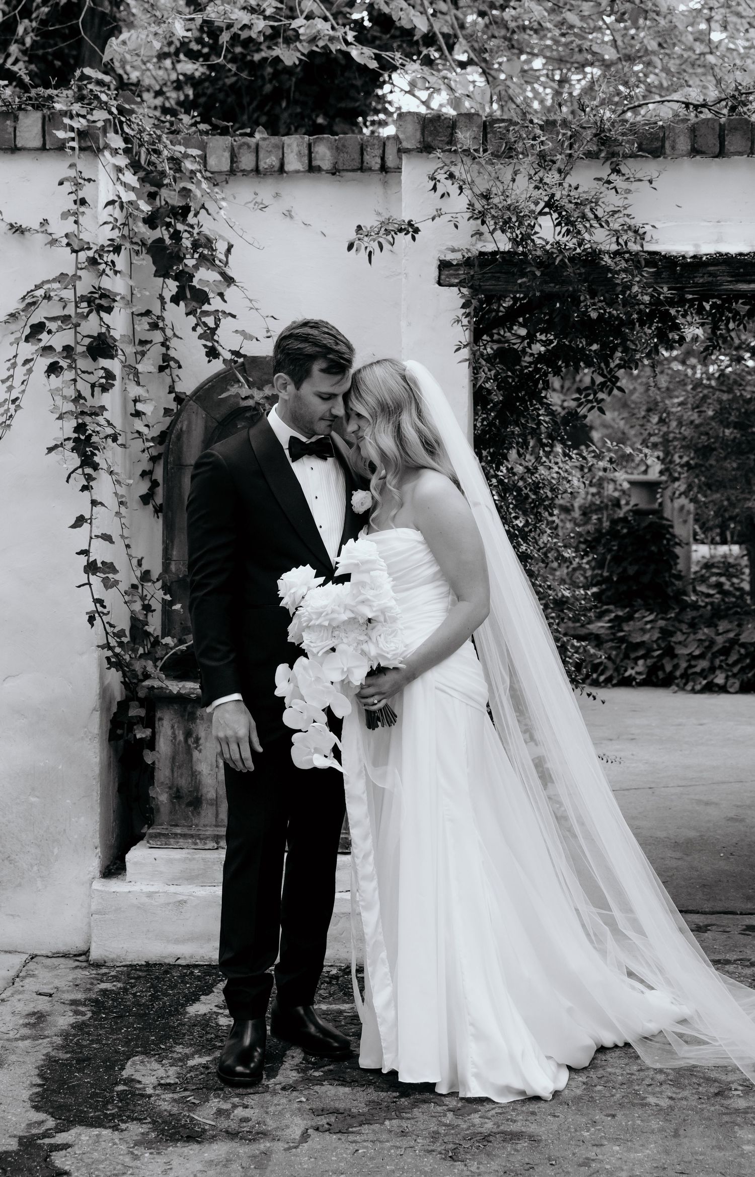 Black and white wedding photo of a bride and groom sharing an intimate moment outdoors.