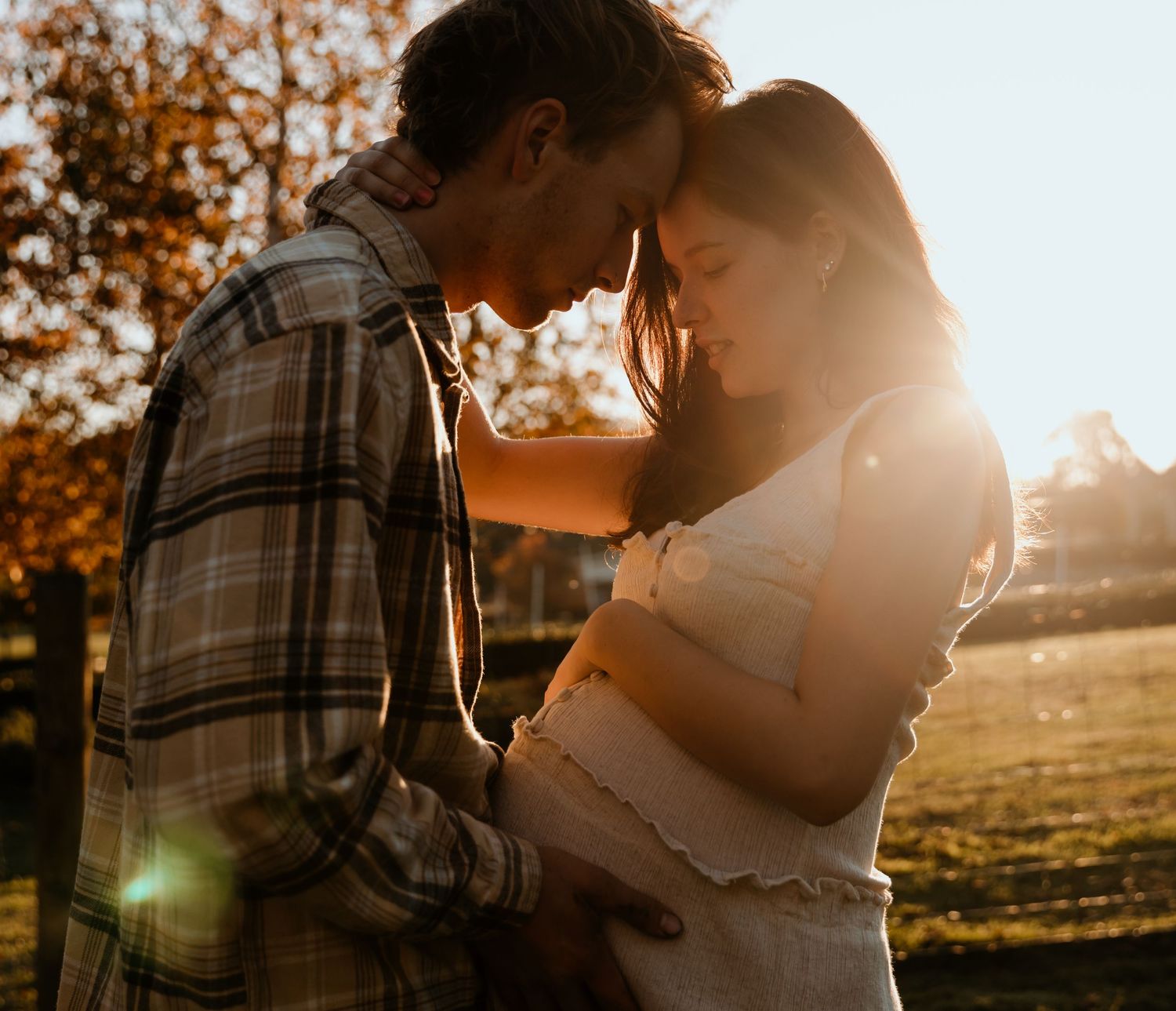 Intimate maternity moment captured in golden sunset light outdoors.