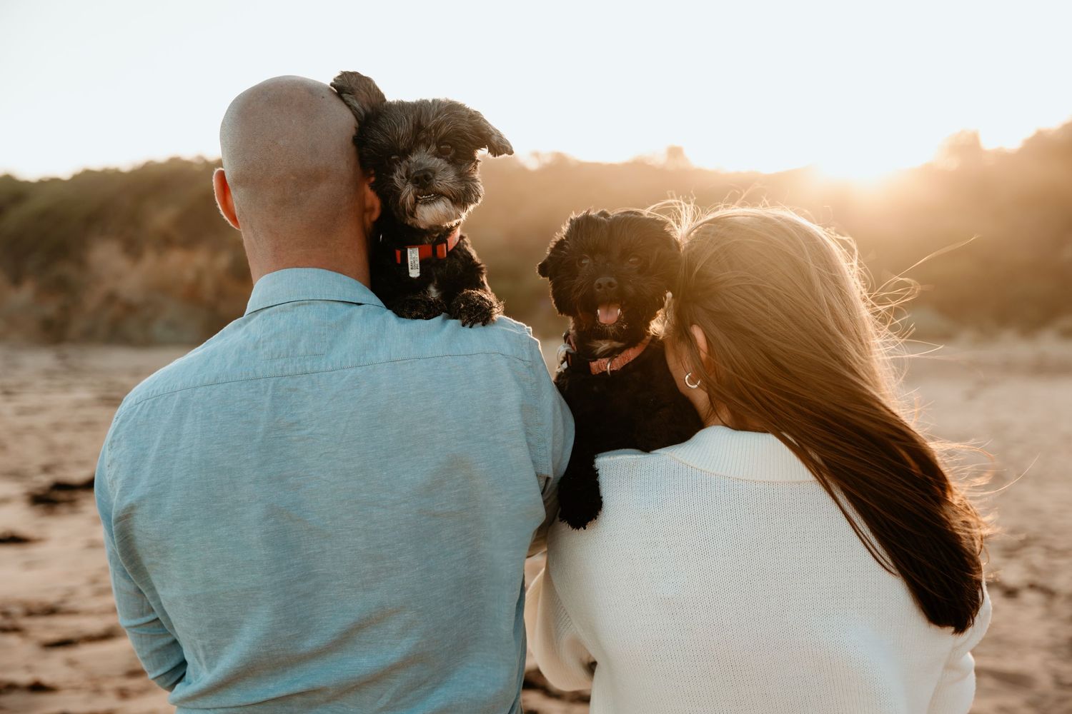 Couple holding their black dogs while enjoying sunset at the beach.