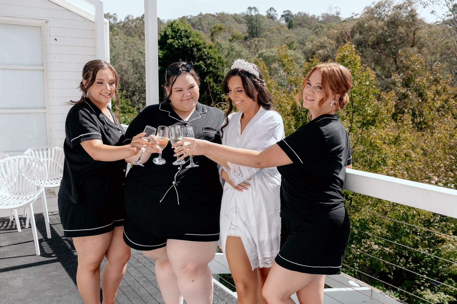 Group of people in black and white outfits celebrating with champagne on a sunny outdoor balcony.