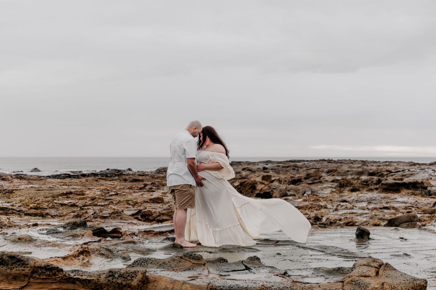 A series of romantic coastal wedding photos showing a couple posing on rocky shores in flowing white attire.