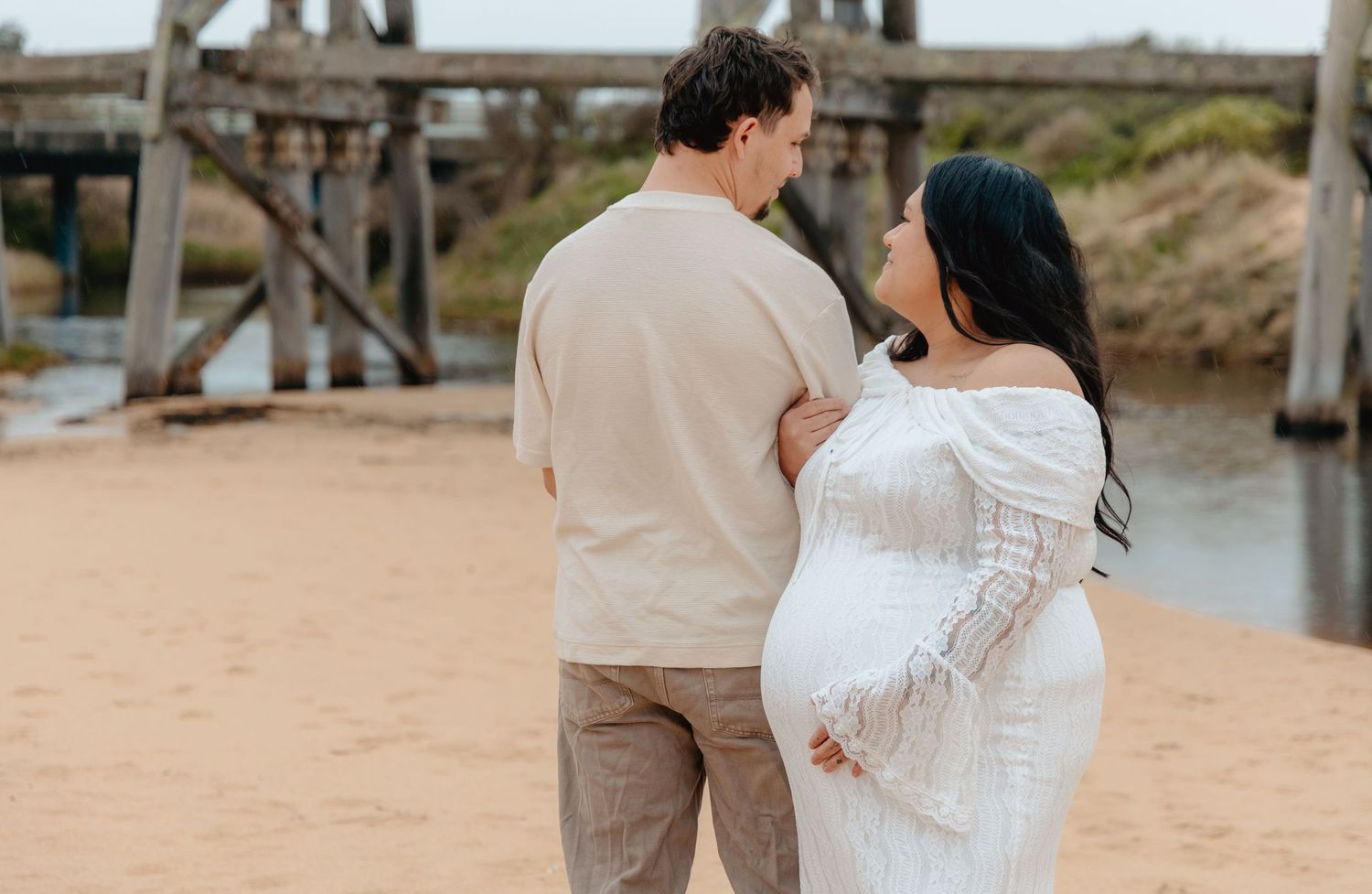A couple in wedding attire embraces on a beach boardwalk during a romantic sunset photoshoot.