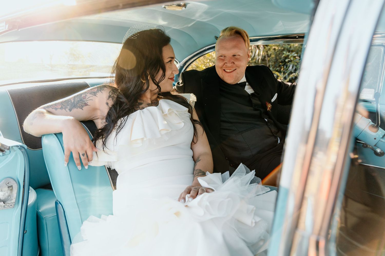 A couple sitting together laughing in a classic turquoise vintage car with white interior on their wedding day.