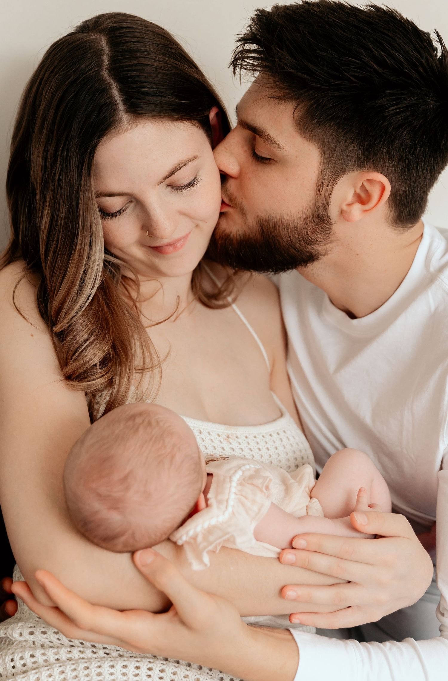 Intimate family moment with newborn baby being held on white bedding.