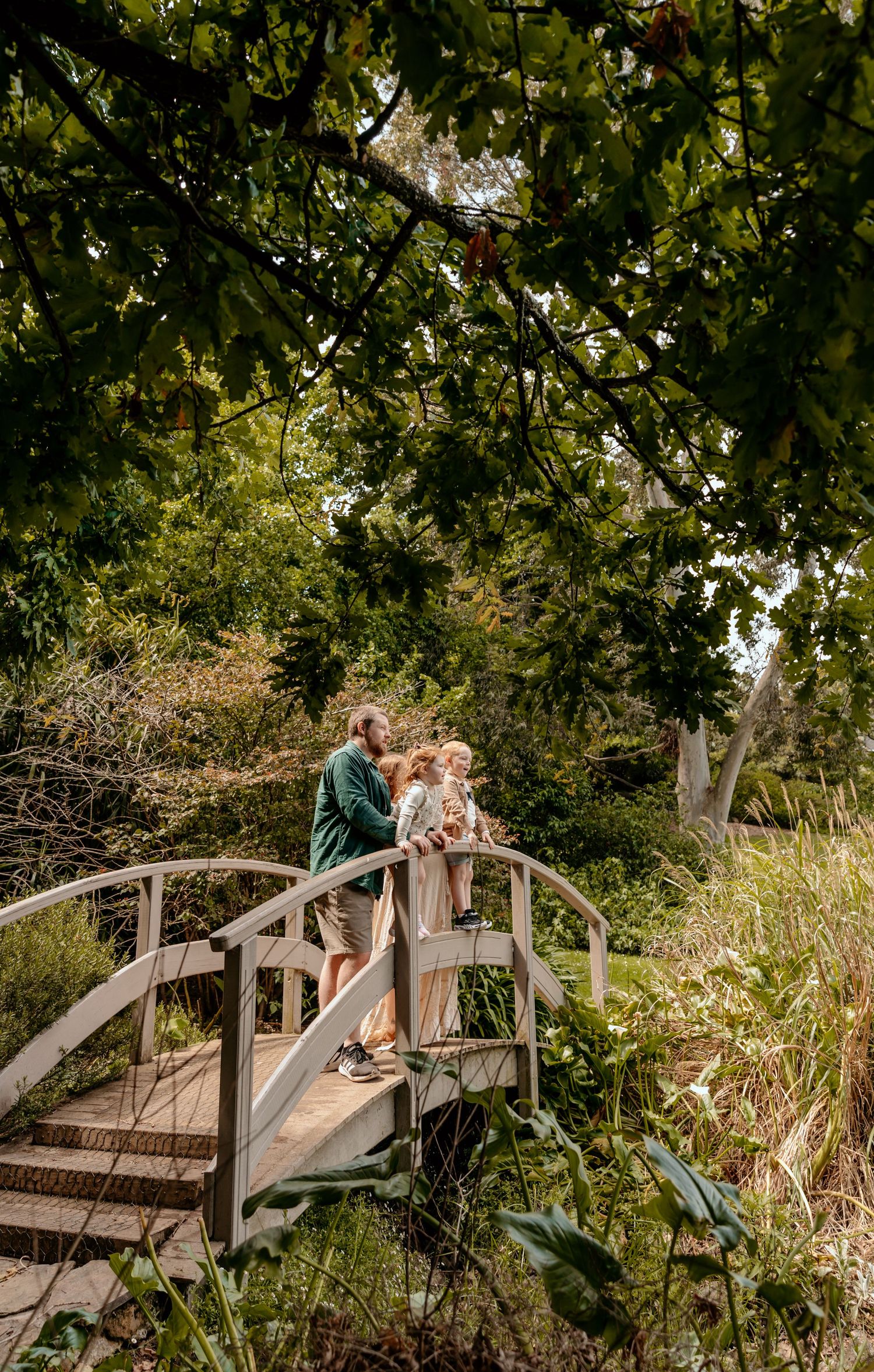 Family standing together on wooden footbridge surrounded by lush garden landscape.