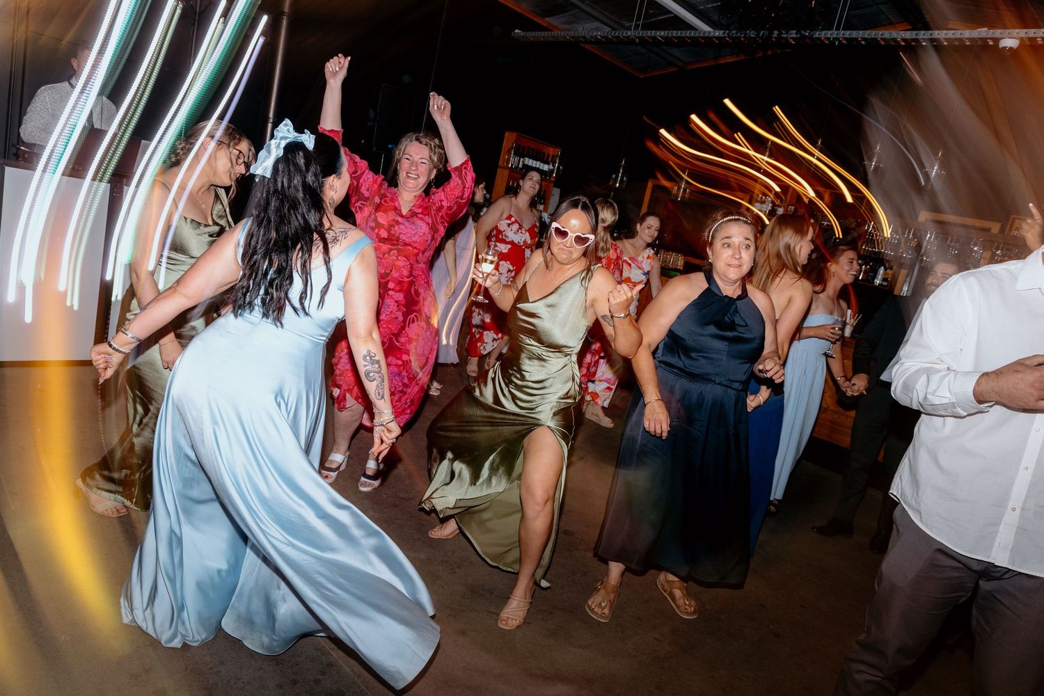 Group of women dancing energetically at a wedding reception party on a dark dance floor.