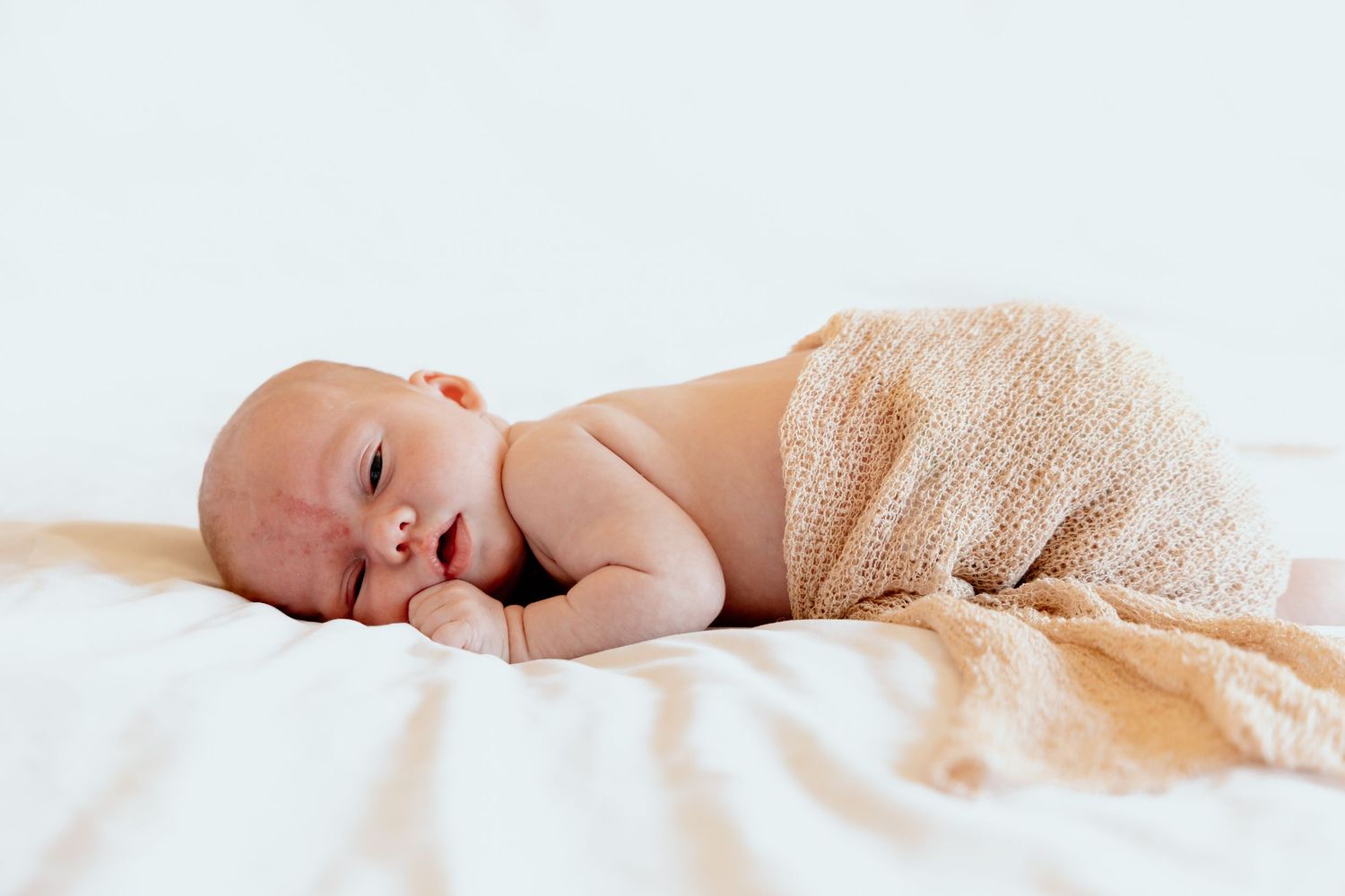 Peaceful sleeping newborn baby wrapped in soft peach blanket on white bedding.