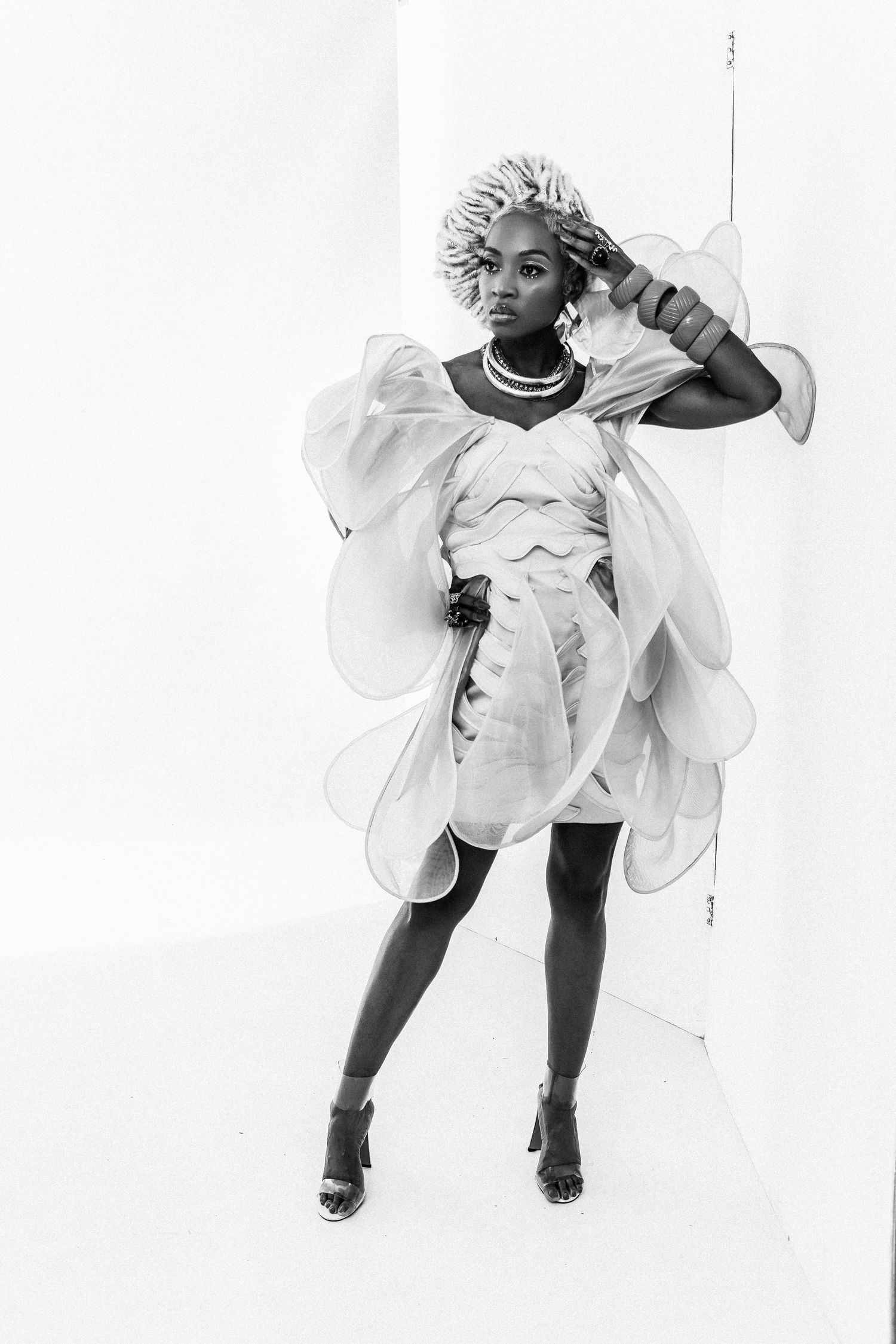 Black and white fashion photo of a woman in an avant-garde white organza dress with sculptural wings and heeled sandals.